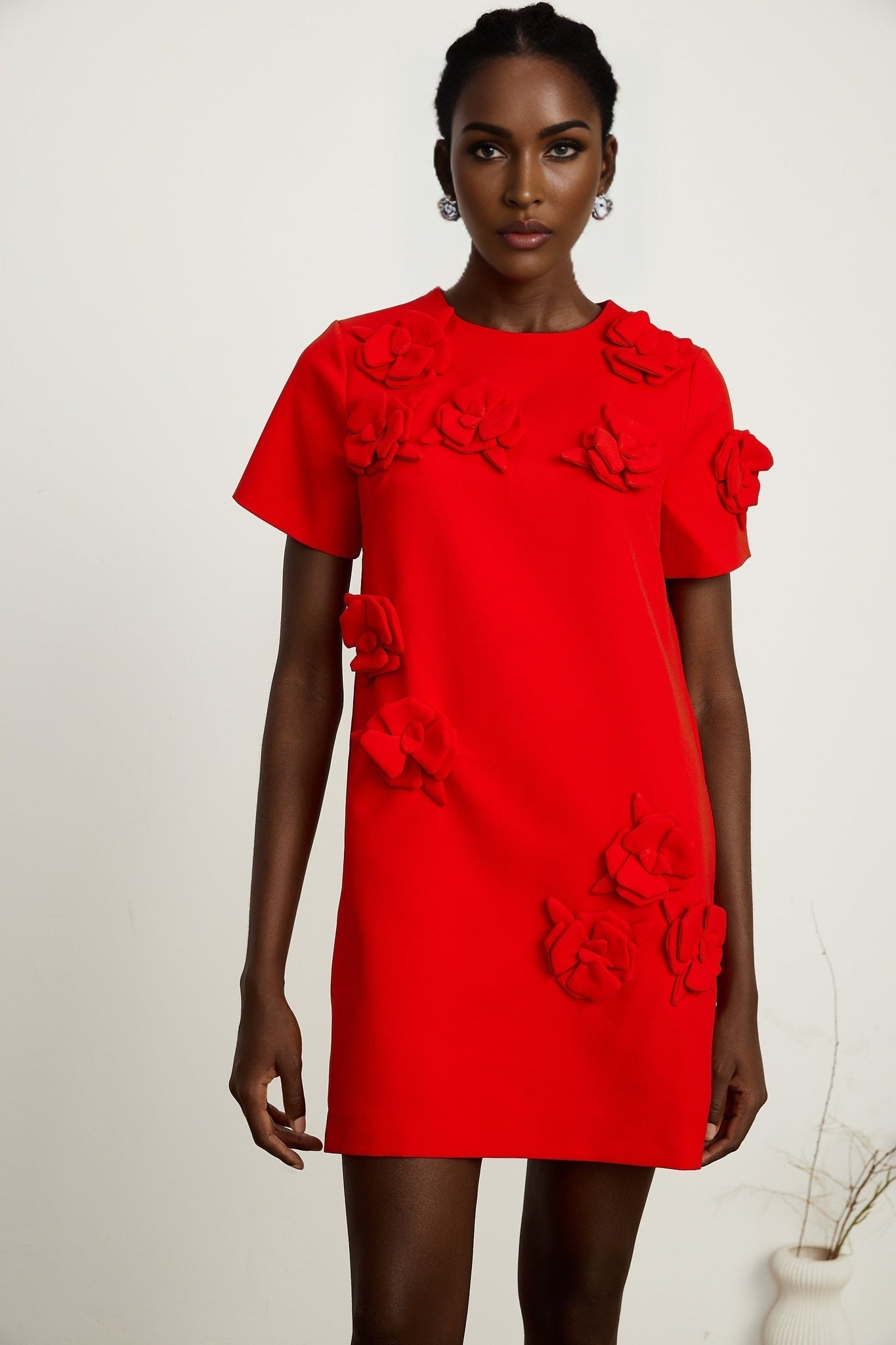 A red mini dress with short sleeves and floral details worn by a model against a plain background