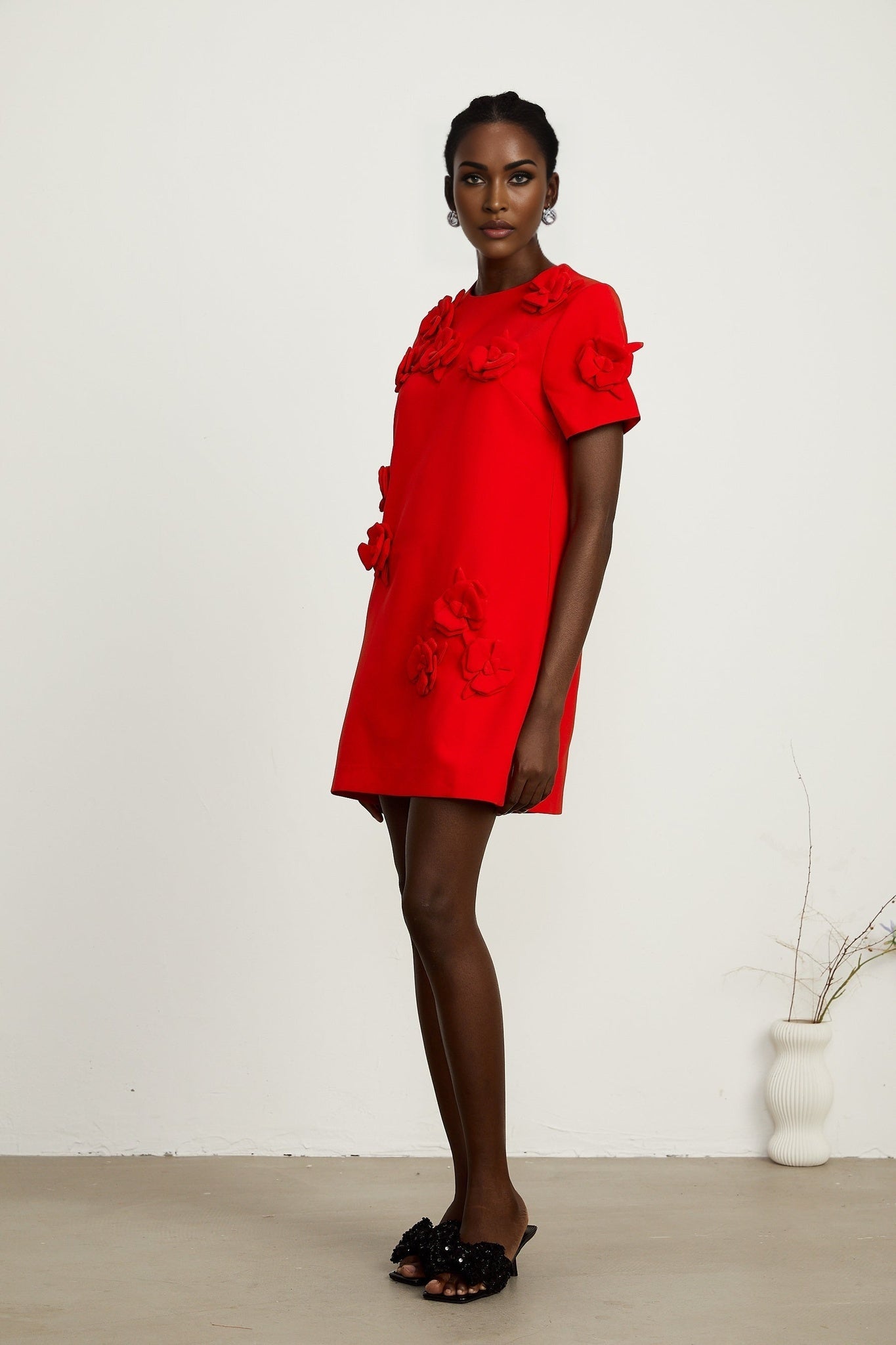 A red mini dress with short sleeves and floral details worn by a model standing against a plain background