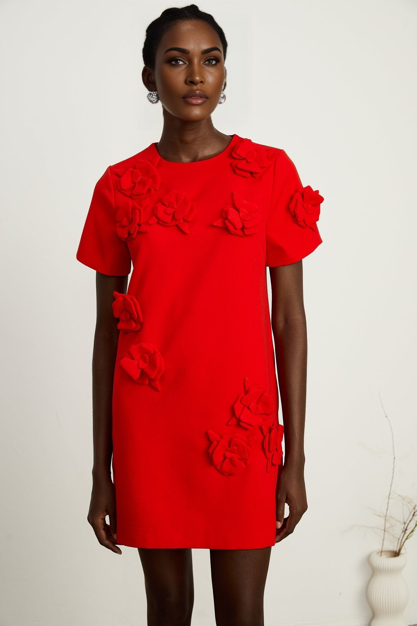 A red mini dress with short sleeves and floral details worn by a model standing against a plain background