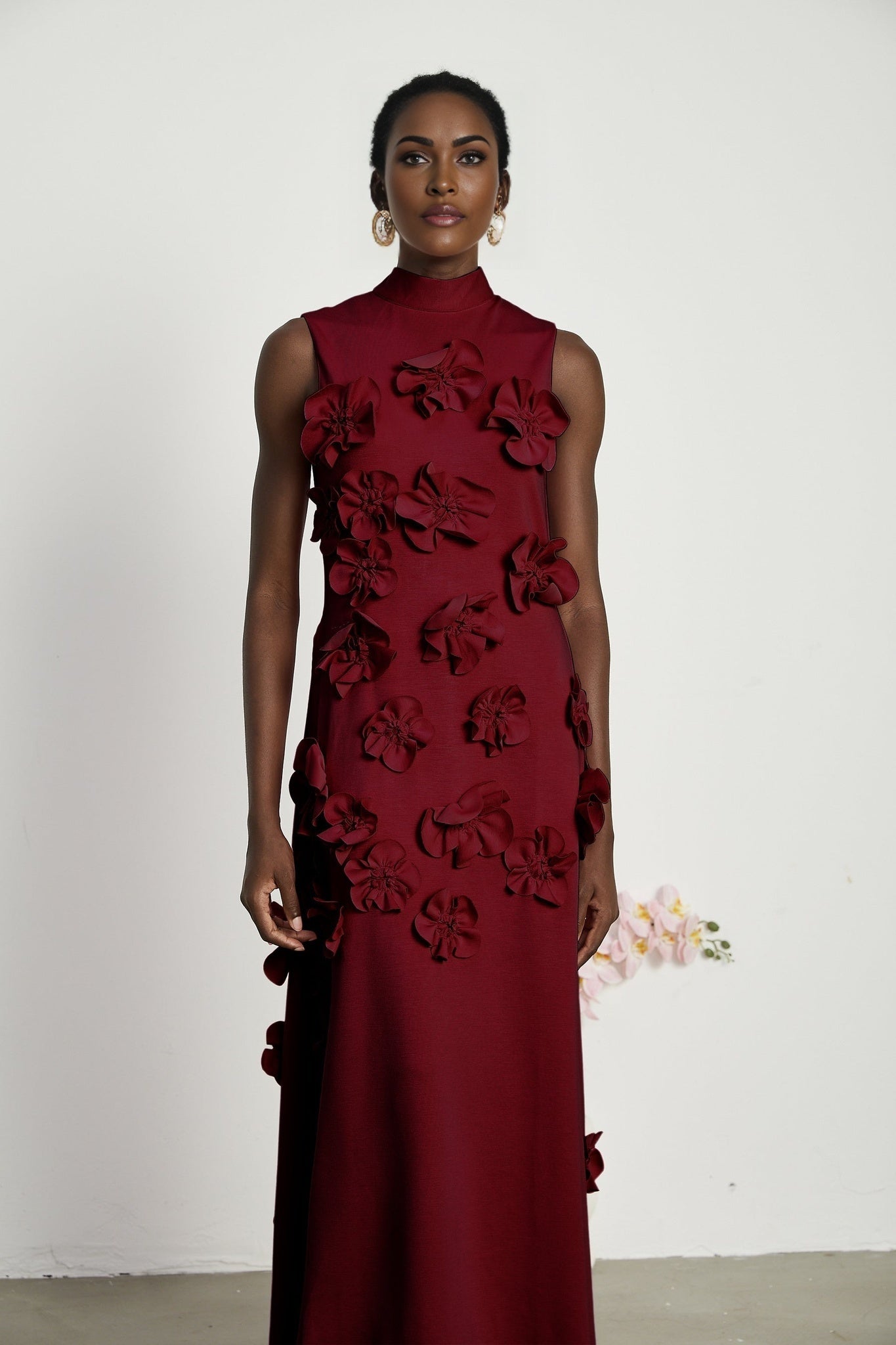 A red sleeveless maxi dress with a bow tie and faux flower embellishments