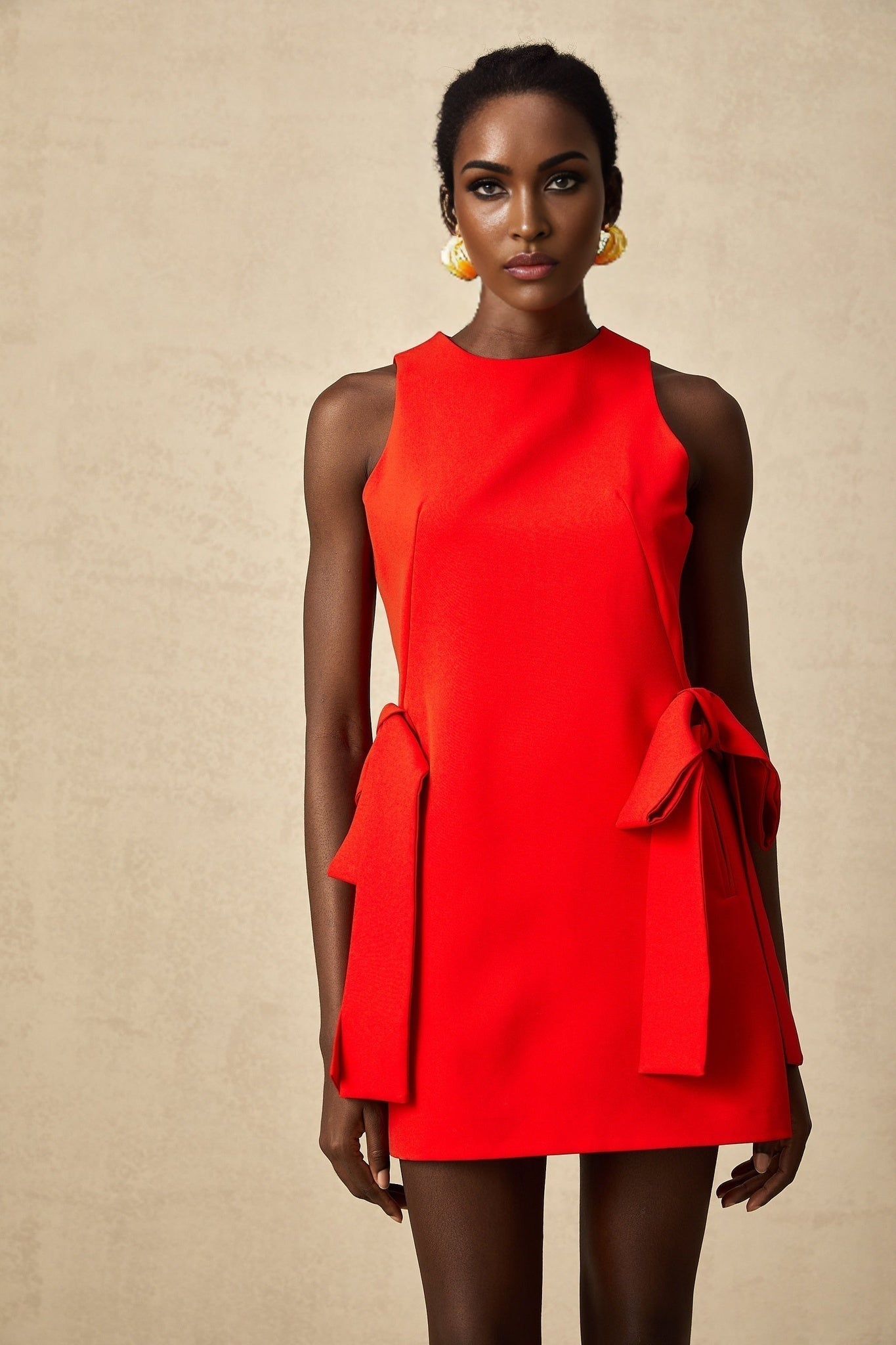 A red sleeveless mini dress with a bow detail worn by a model