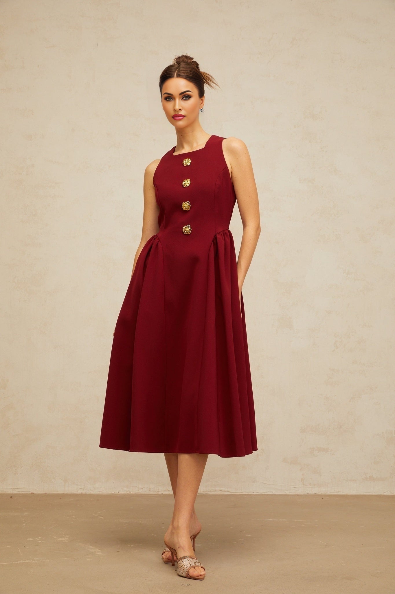 A red sleeveless tank dress with a floral pattern featuring a pleated midi skirt and a fitted bodice The dress has an allover flower motif in a contrasting color against the red background