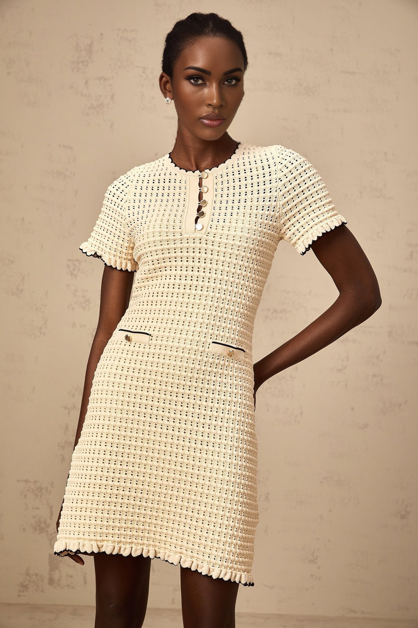 A short beige knit dress with ruffled details and a pointelle pattern featuring a mini length and neutral tones