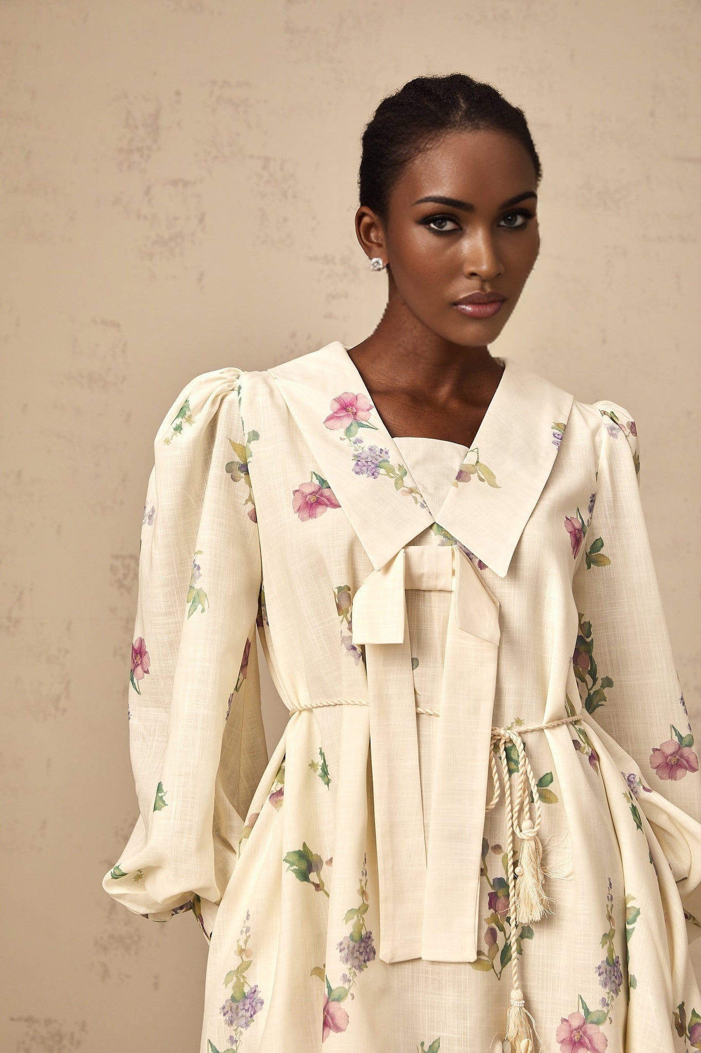A short beige mini dress with a floral print pattern and a bow detail at the neckline