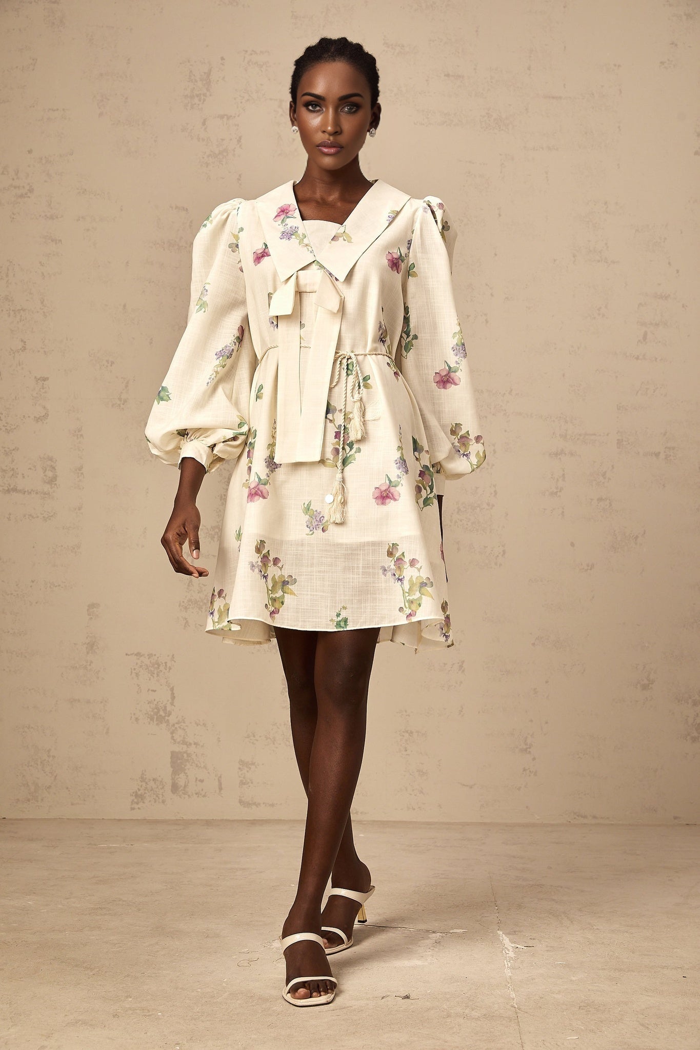A short beige mini dress with a floral print pattern and a decorative bow at the waist