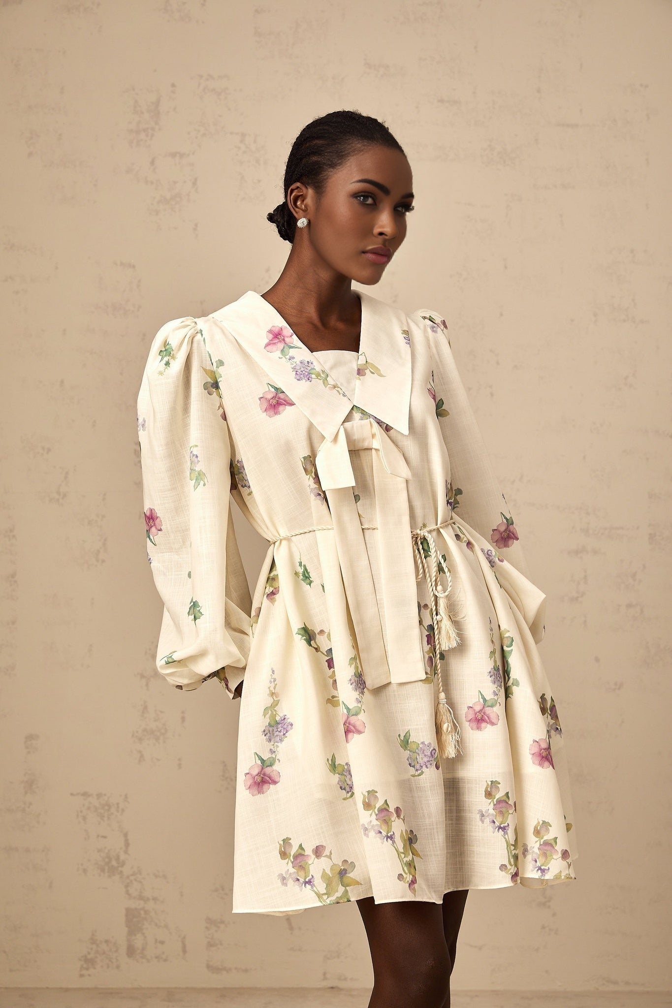 A short beige mini dress with a floral print pattern and a decorative bow detail at the neckline