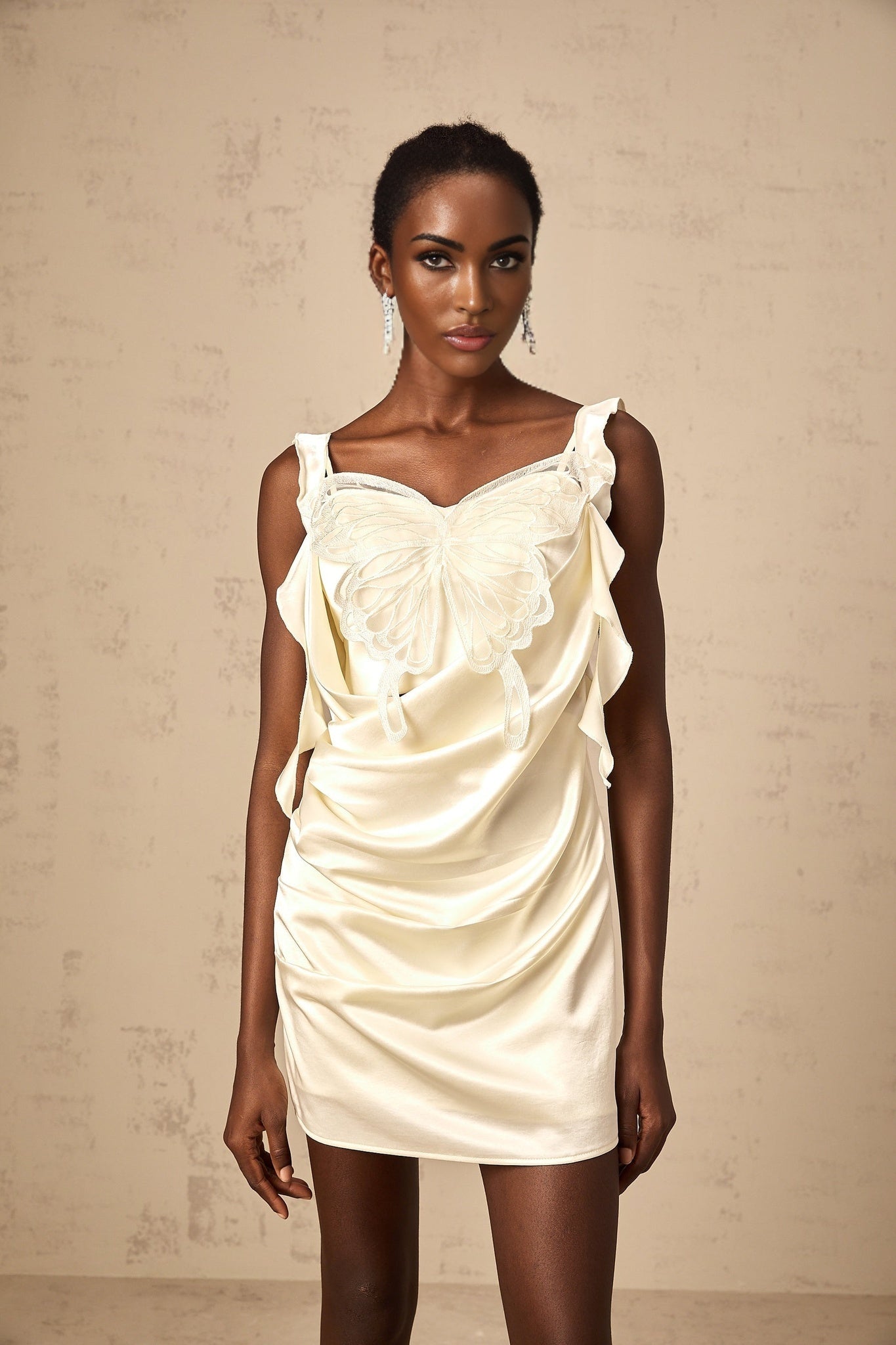 A short beige mini dress with butterfly patterns and draped fabric design featuring neutral tones and a flattering silhouette
