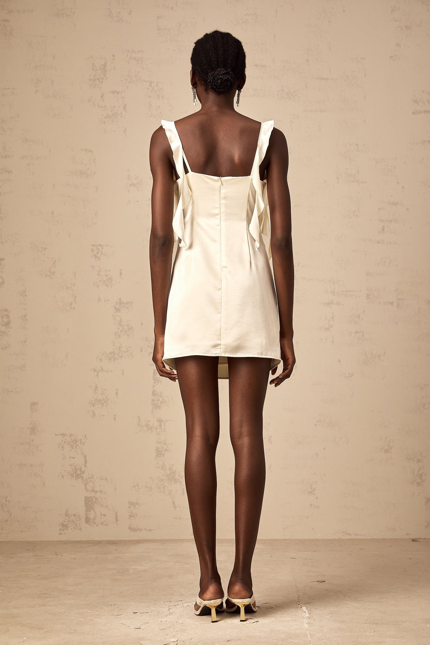 A short beige mini dress with butterfly prints and draped fabric details featuring a sleeveless design and a flowing silhouette