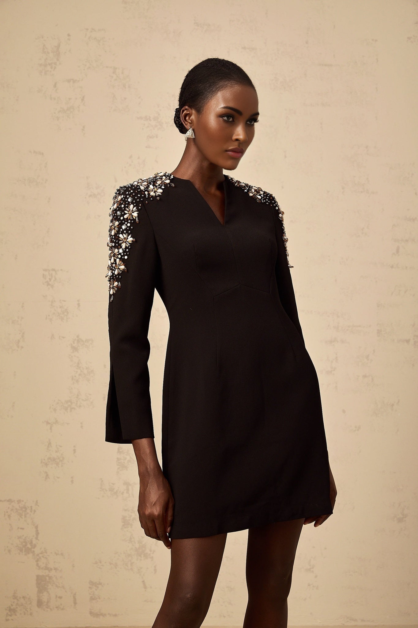 A short black mini dress with a split neckline and embellished details worn by a model against a plain background