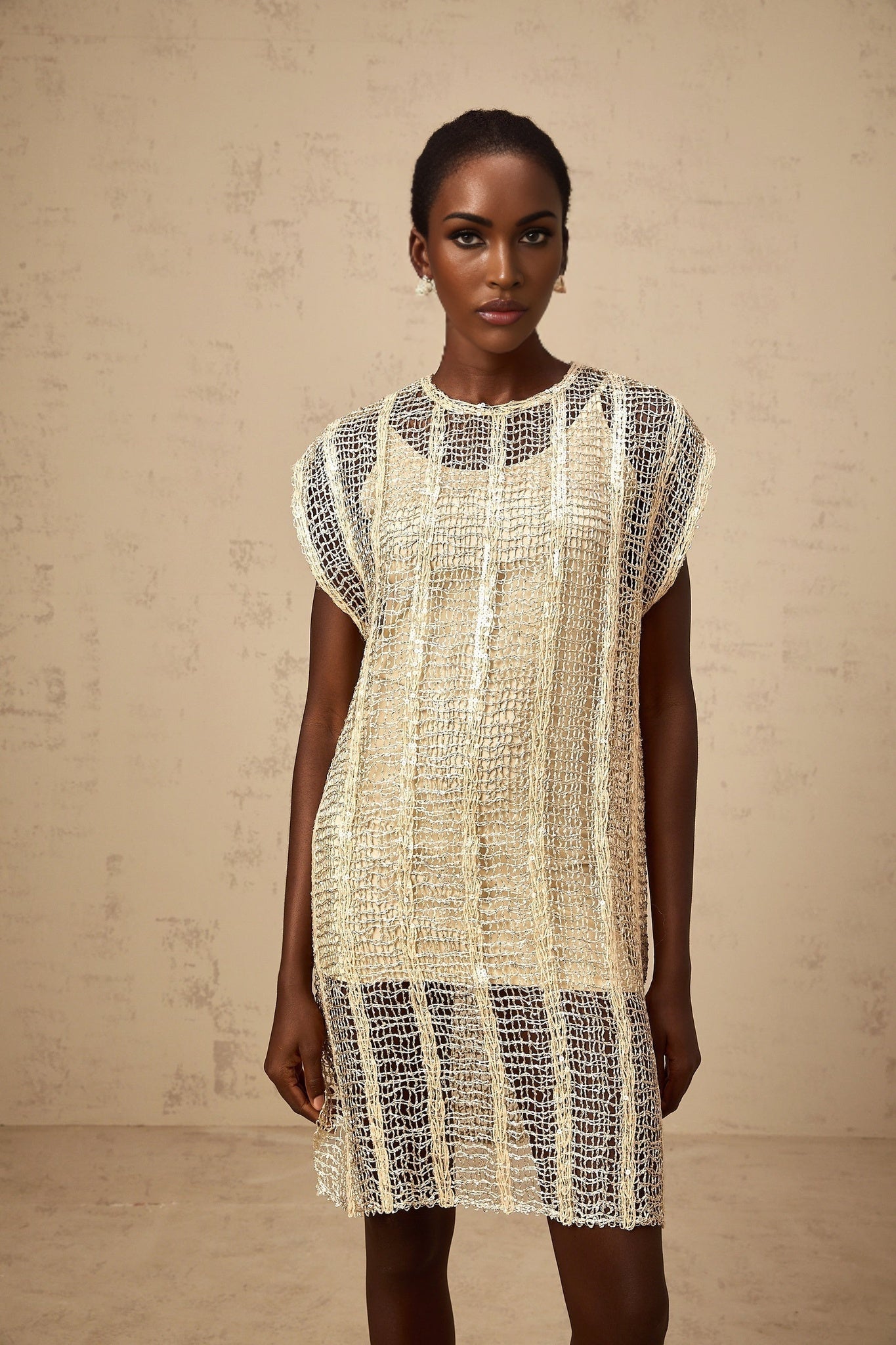 A short gold mini dress with sequin embellishments and cut out details on a model
