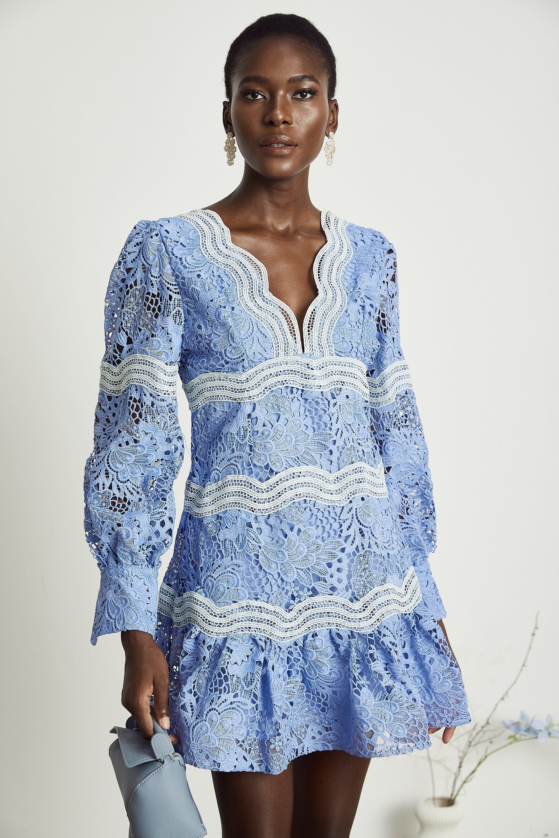 A short ivory mini dress with floral embroidery and a Vneckline worn by a model standing against a plain background