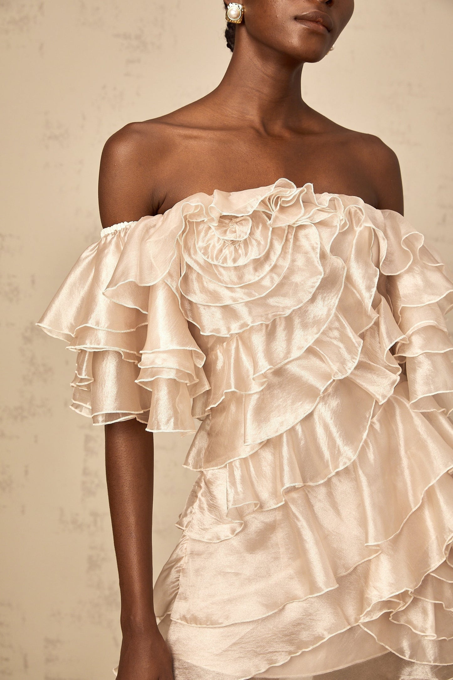 A short neutral colored mini dress with an asymmetric design featuring a flounce detail and a cerise pink accent