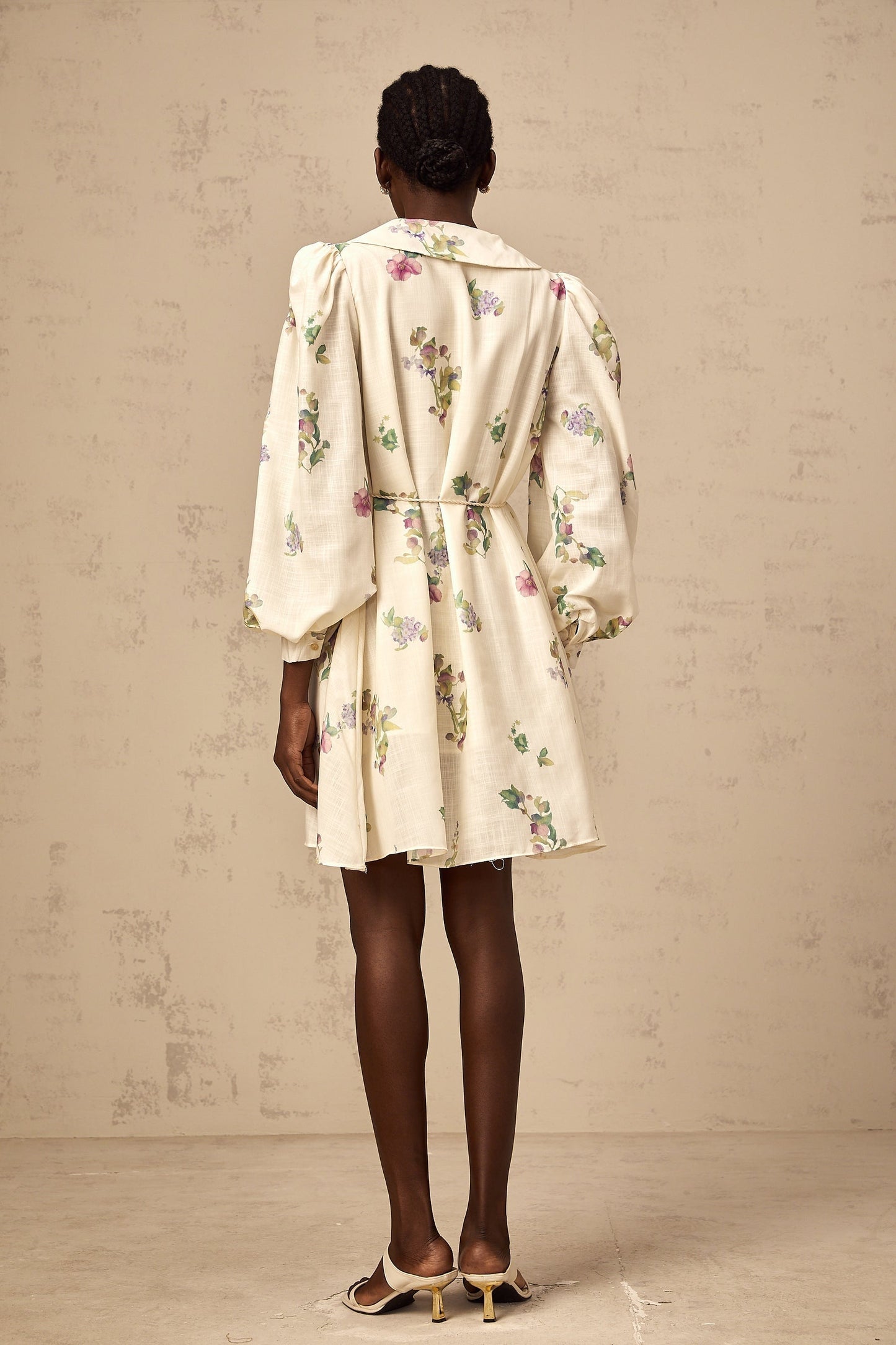 A short neutraltoned mini dress with a floral print pattern and a bow detail at the neckline