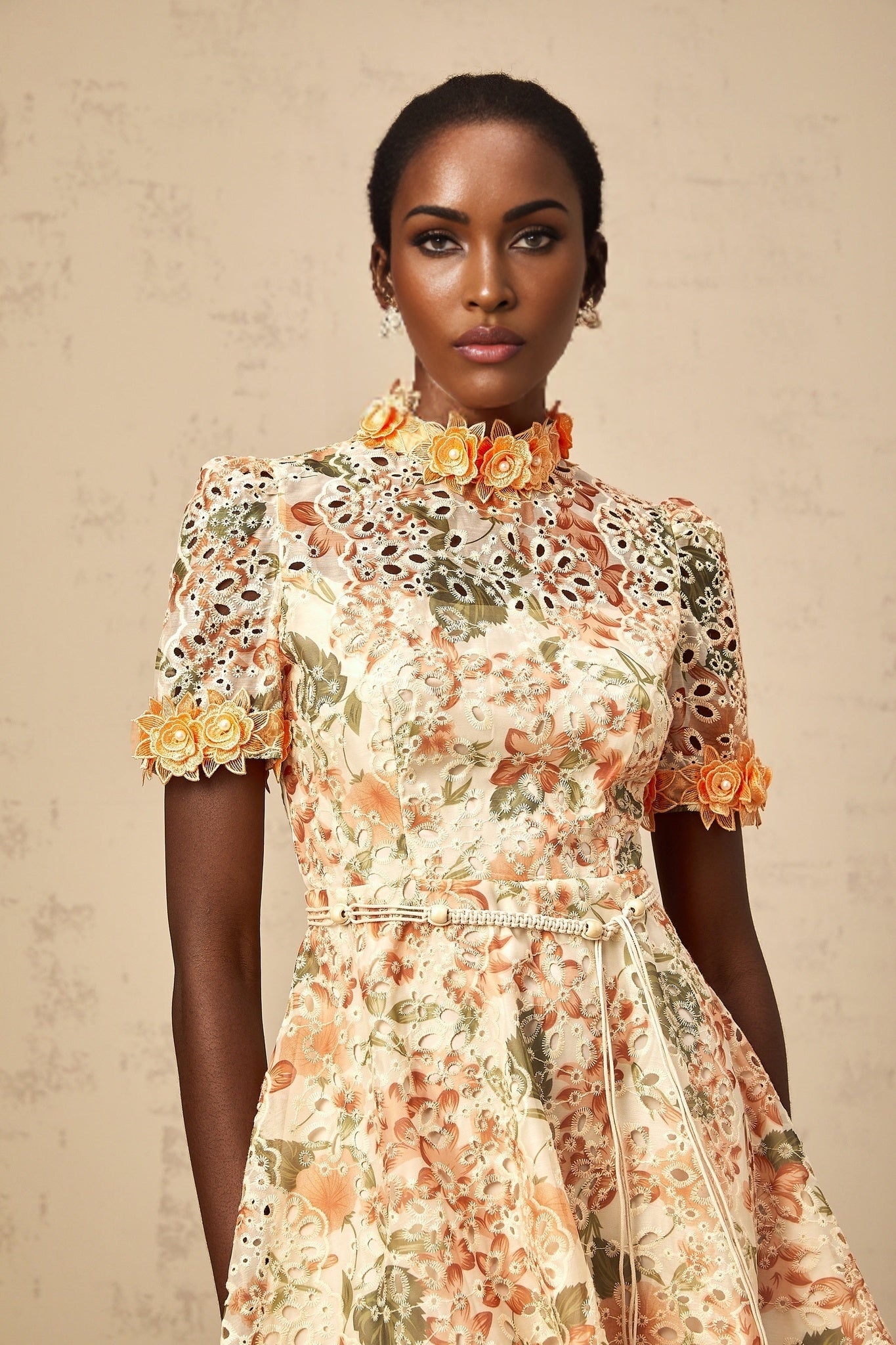 A short orange mini dress with floral embroidery and embellishments featuring a fitted silhouette and delicate flower patterns stitched onto the fabric