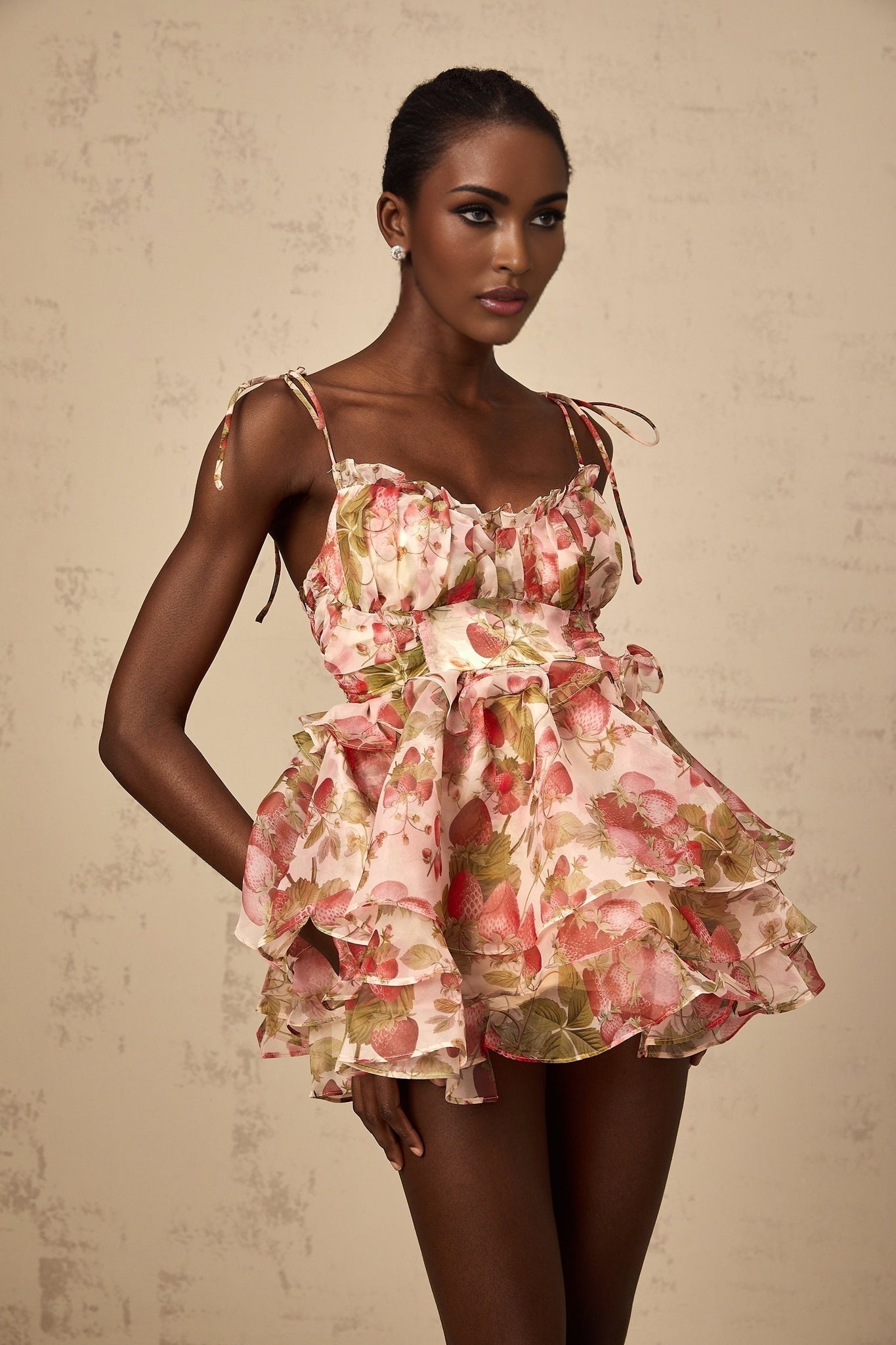 A short pink dress with a strawberry print pattern featuring tiered ruffles and a fitted bodice
