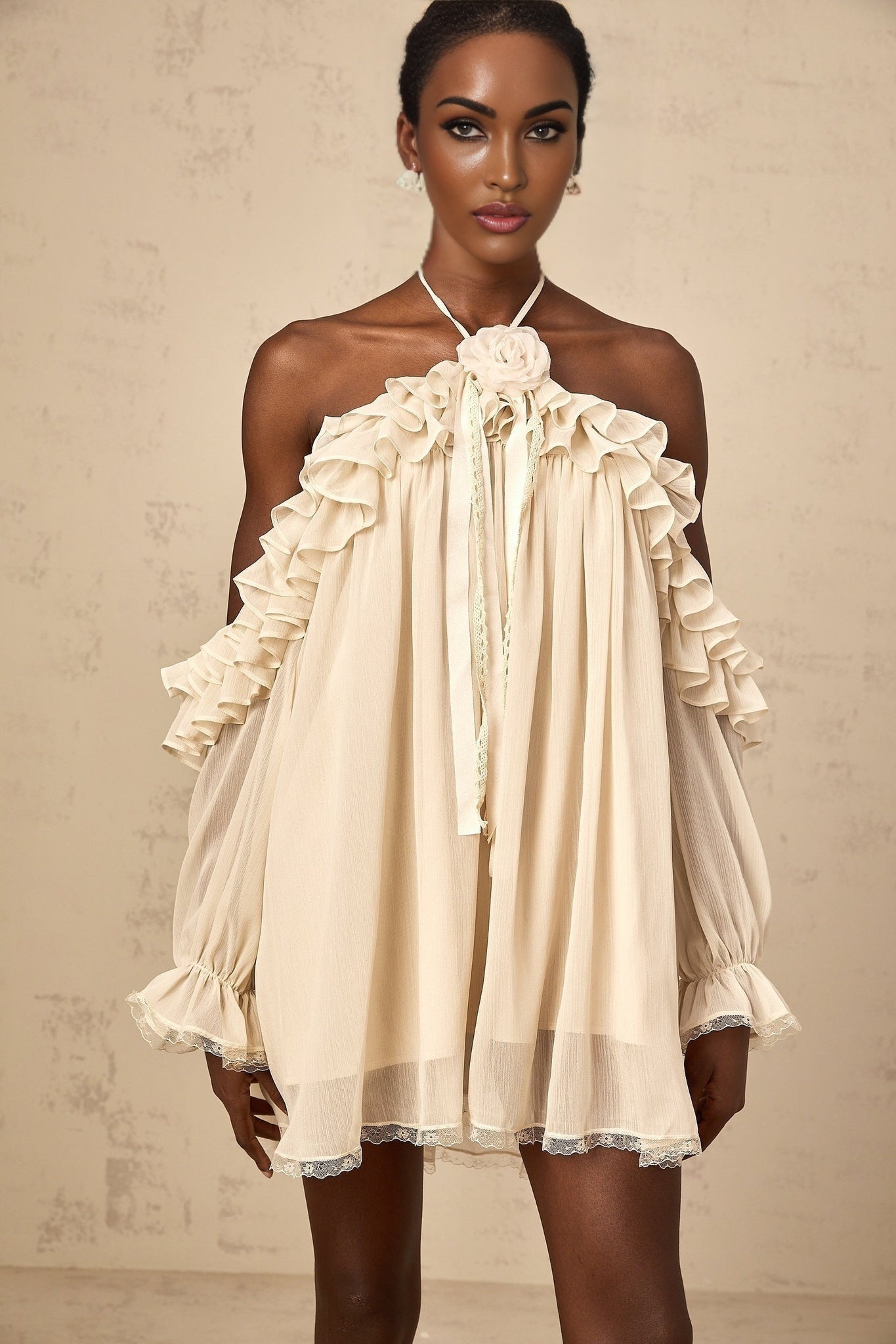 A short sleeveless dress in neutral tones with ruffled details and floral appliques decorating the bodice and skirt