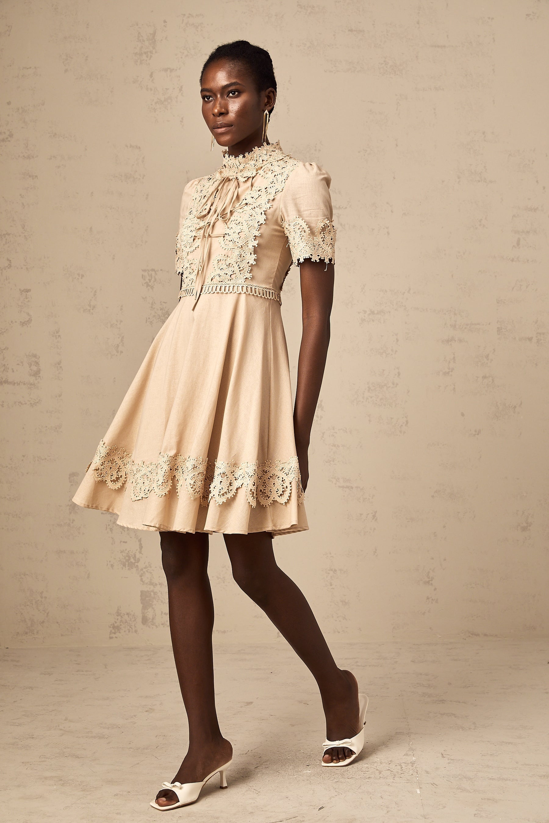 A short sleeveless dress with a flared skirt made of corded lace fabric featuring a delicate floral pattern and scalloped edges
