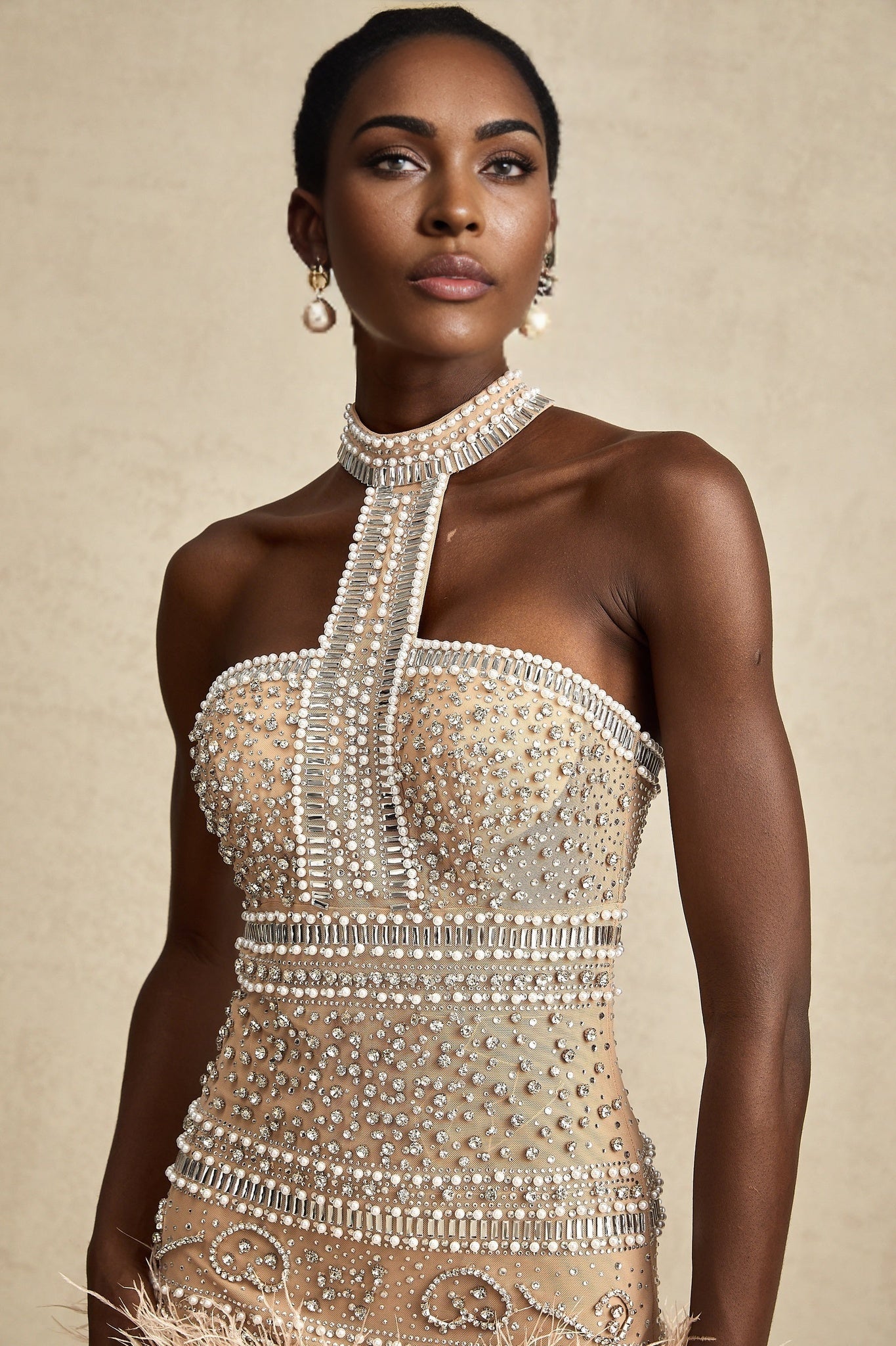 A short sleeveless mini dress with crystal embellishments and feather trim along the hem featuring a Madeleine style silhouette