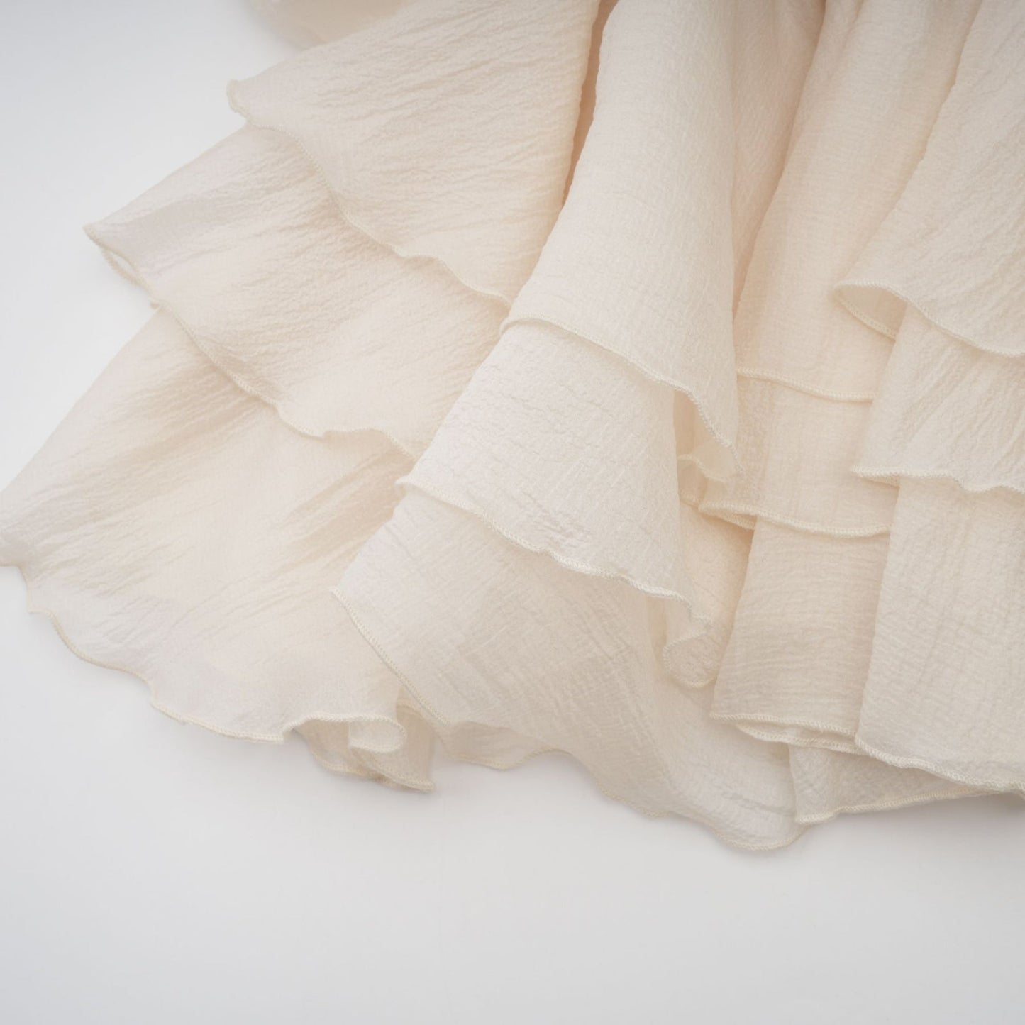 A short sleeveless tiered mini dress in neutral tones with floral applique details throughout the fabric