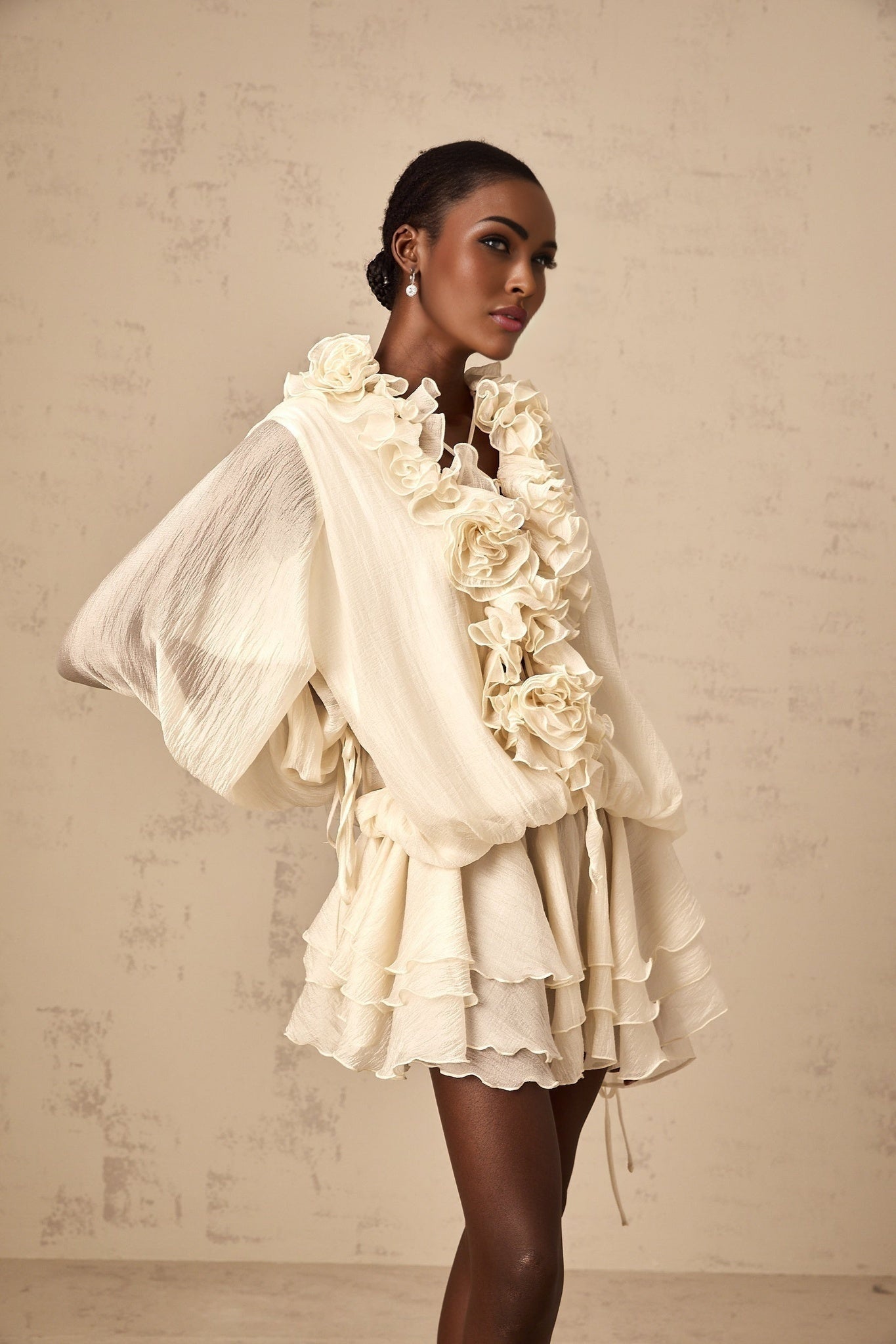 A short tiered mini dress in neutral tones featuring floral applique details and a feminine silhouette called Zephyrine
