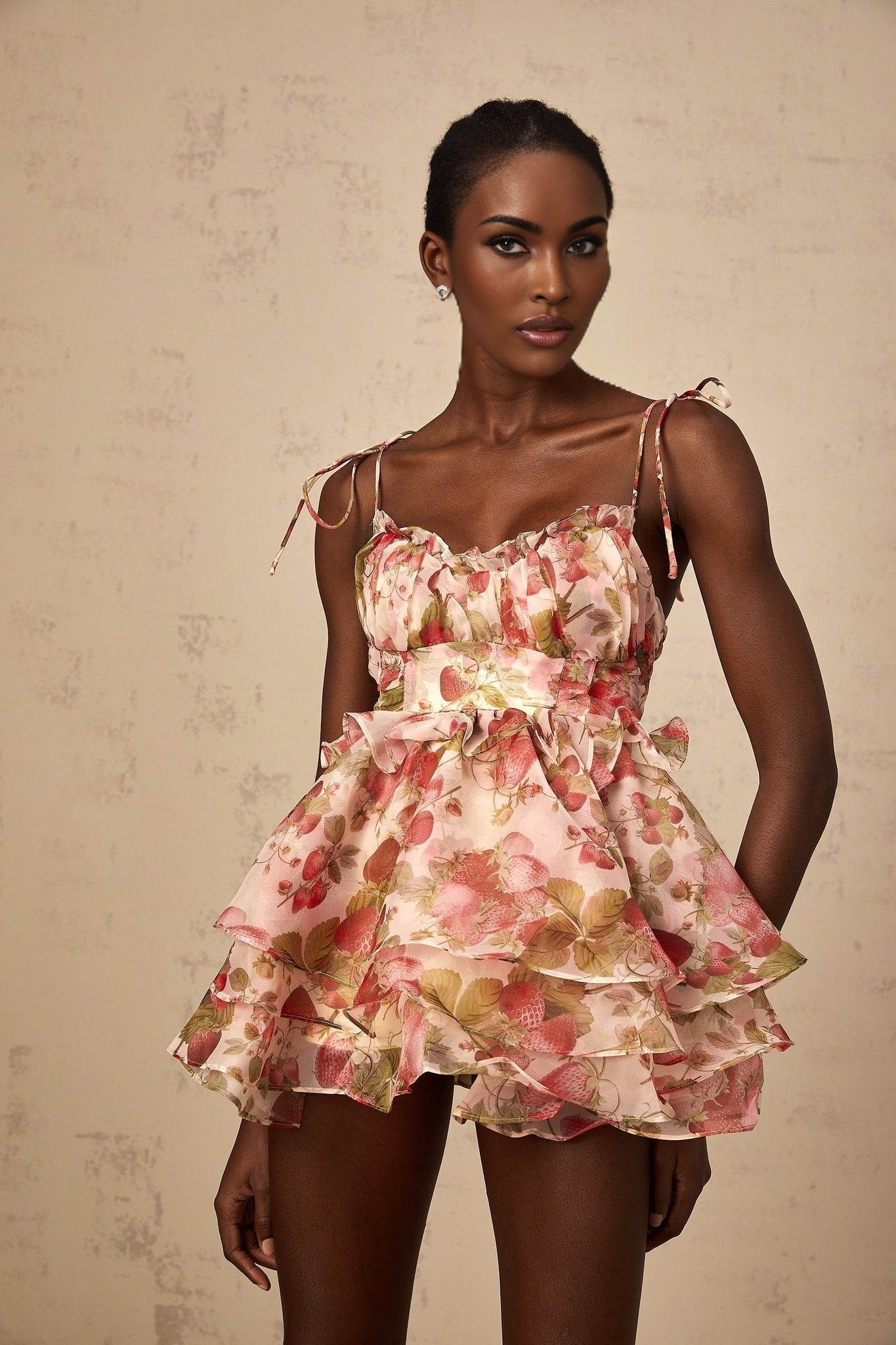 A short tiered mini dress with a strawberry print pattern featuring a light background and red strawberries scattered throughout the fabric