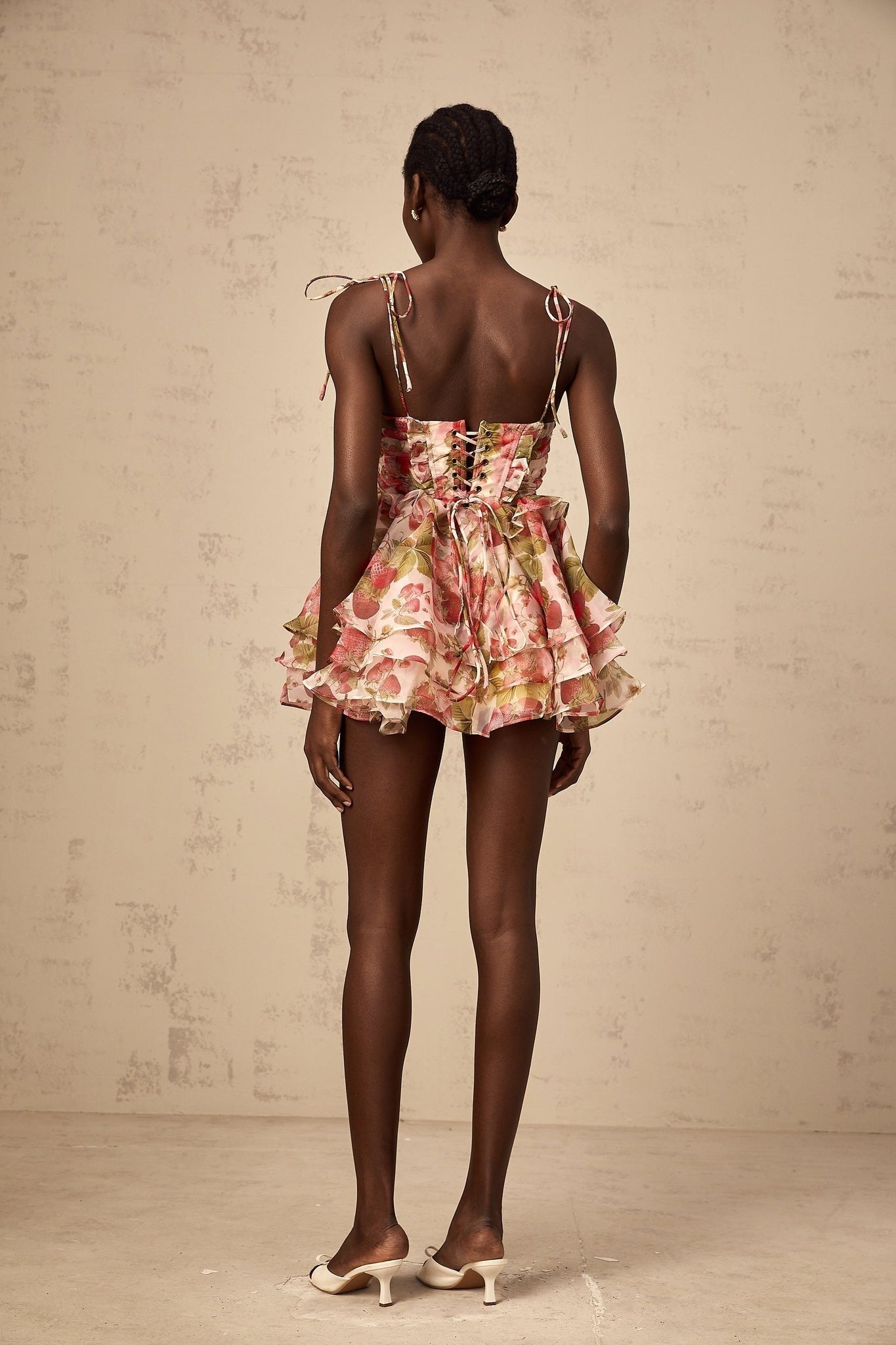 A short tiered mini dress with a strawberry print pattern featuring a light background and red strawberries scattered throughout the fabric
