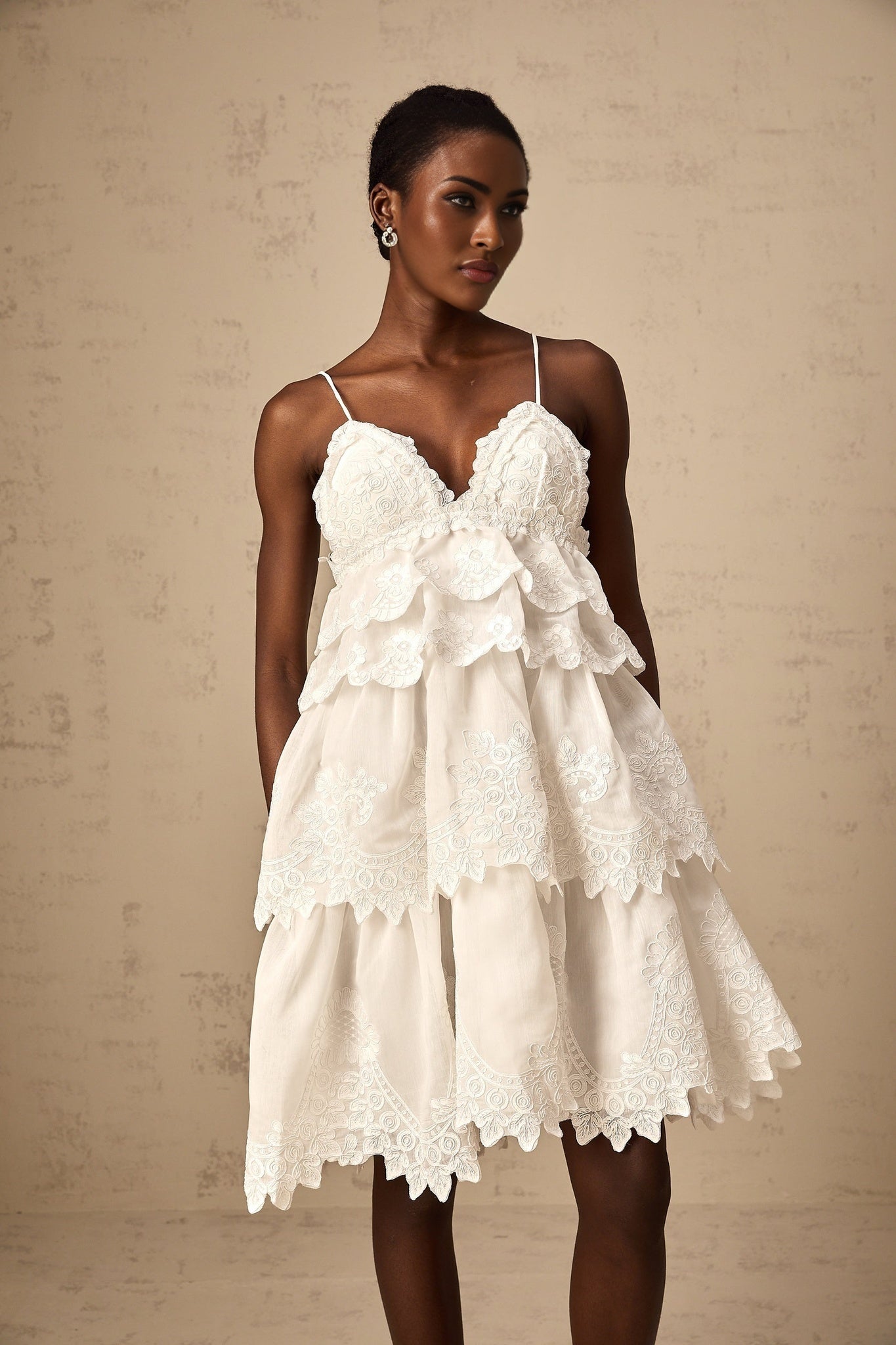 A short white dress with tiered layers made of delicate guipure lace featuring intricate floral patterns and a mini length silhouette