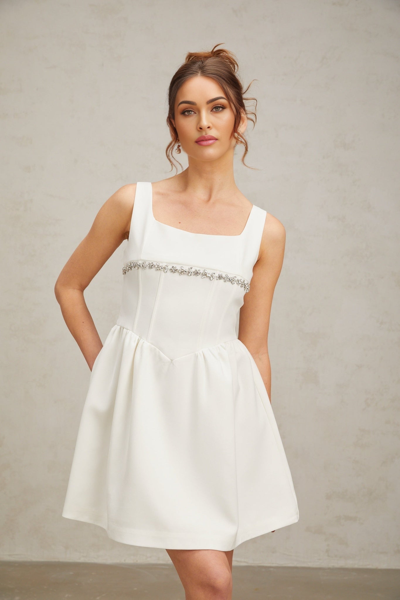 A short white mini dress adorned with crystal embellishments featuring a fitted silhouette and sparkling Flavia design