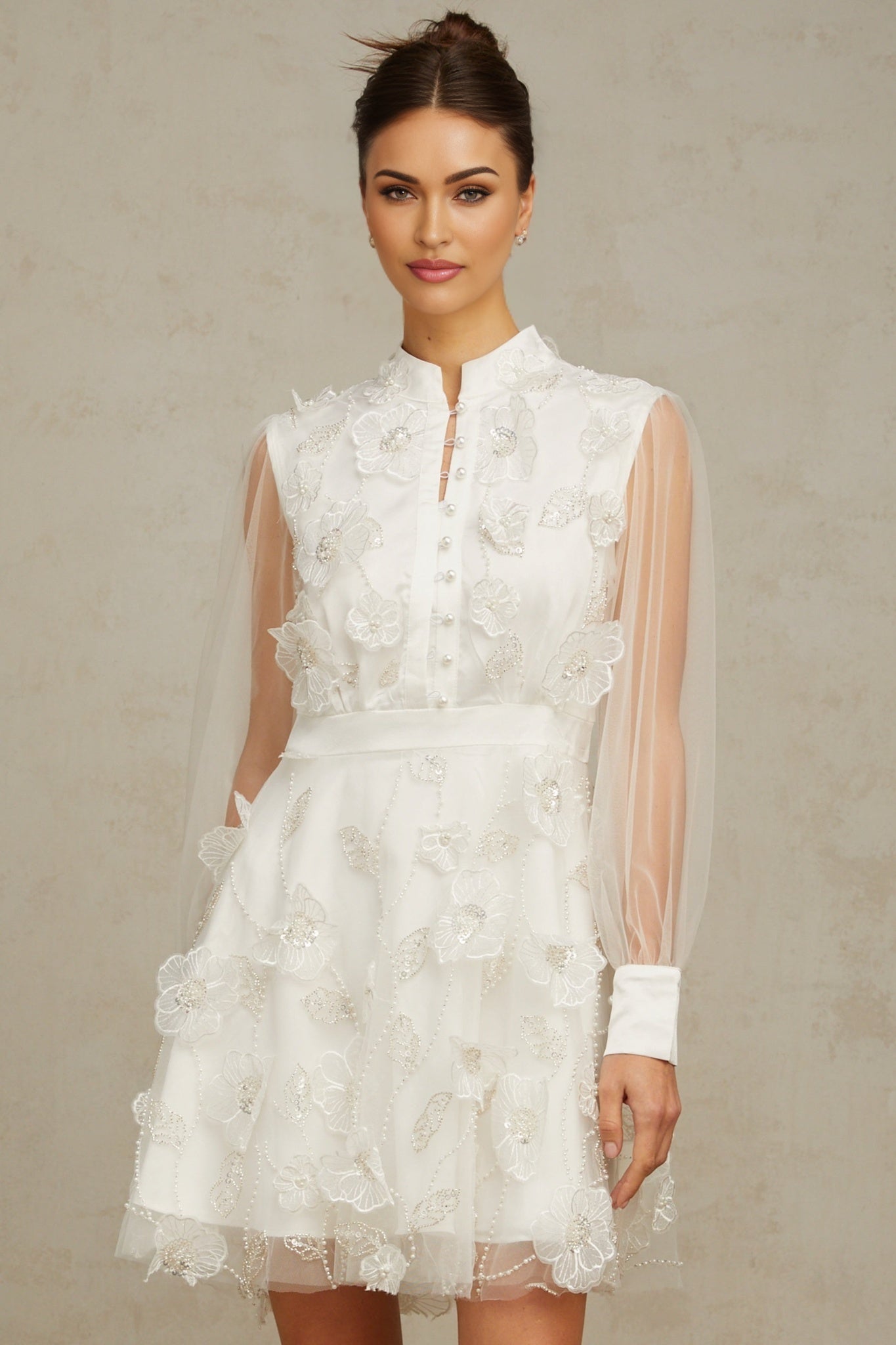 A short white mini dress with a textured 3D petal design made of tulle fabric featuring a floral inspired pattern throughout