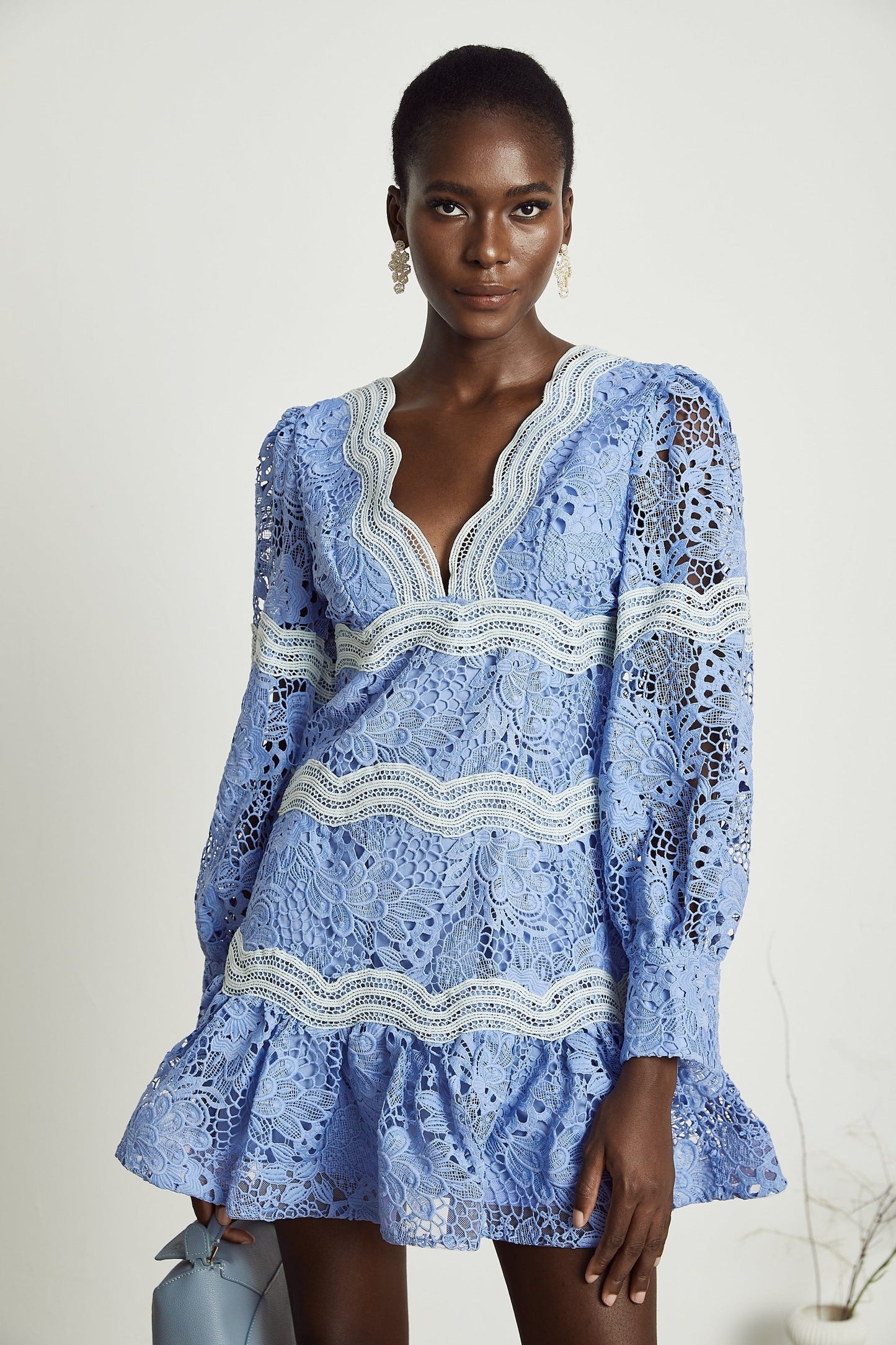 A short white mini dress with a Vneck and colorful floral embroidery details worn by a model against a plain background