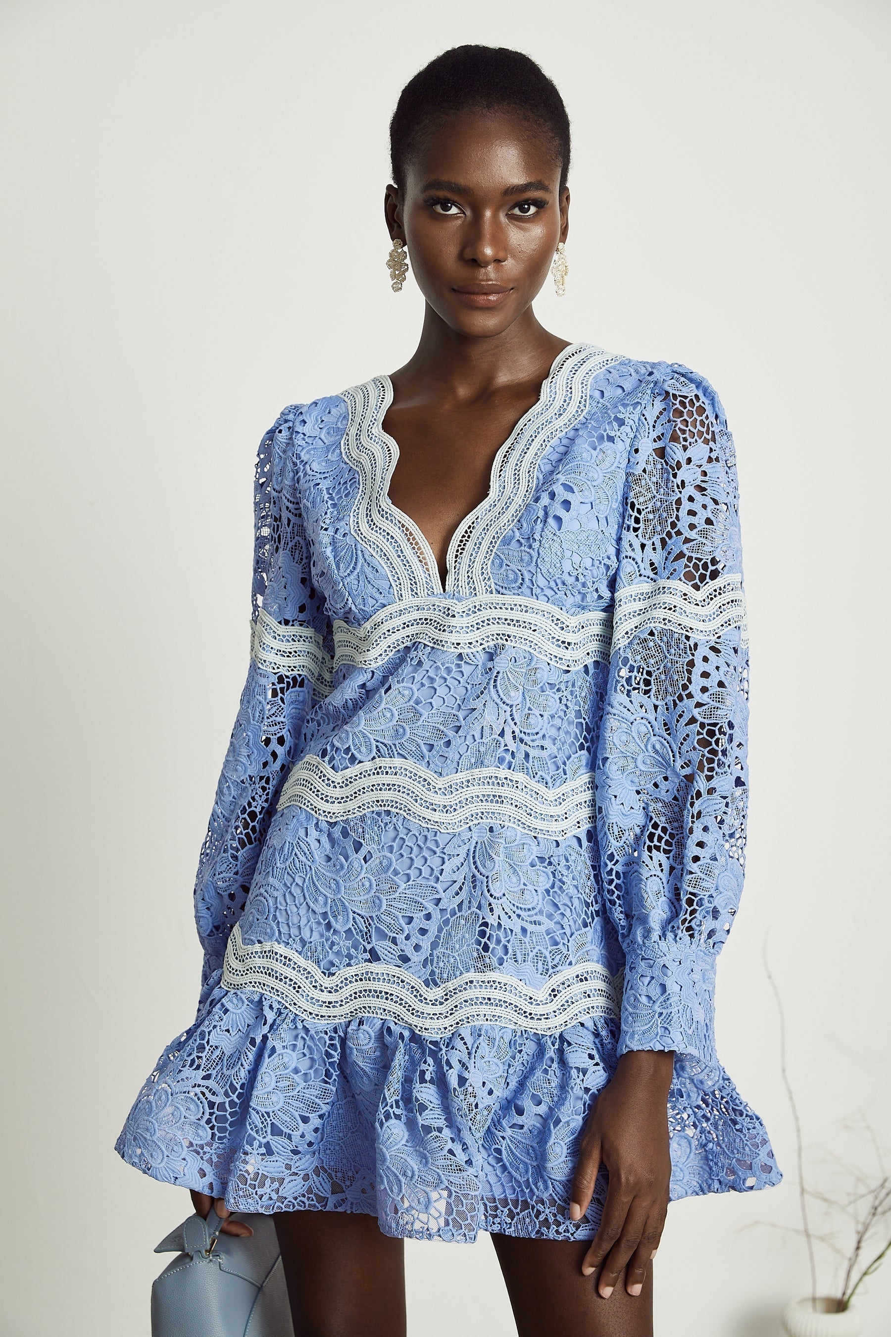A short white mini dress with a Vneck and colorful floral embroidery details worn by a model against a plain background