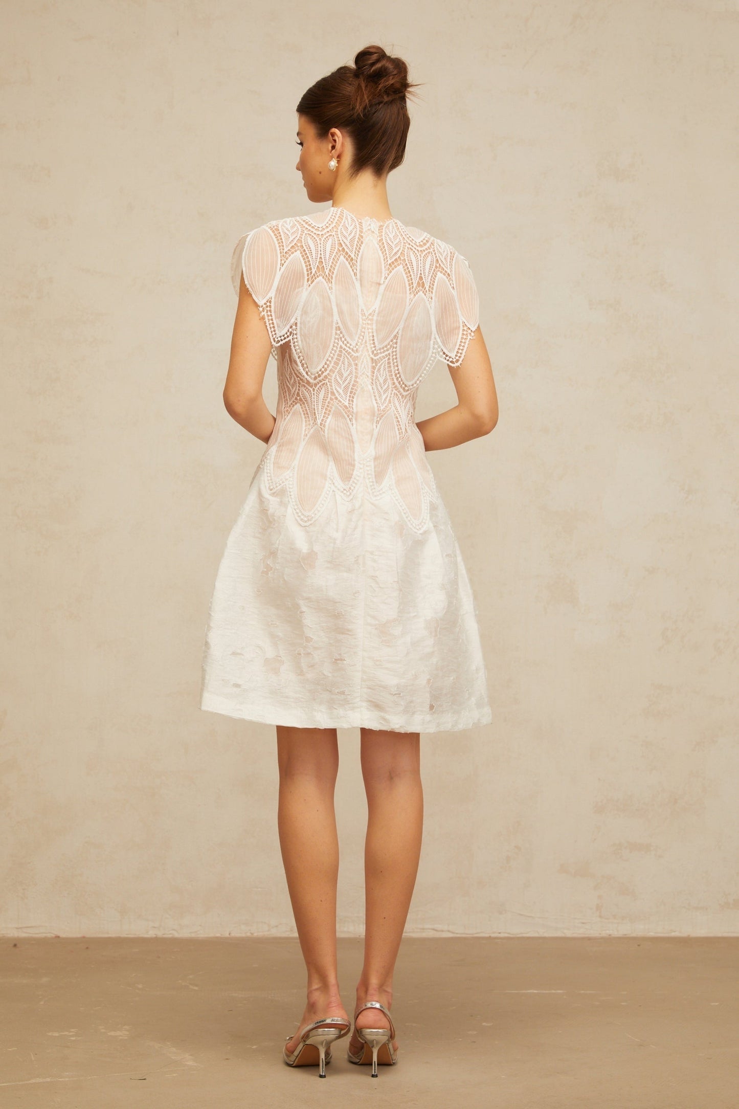 A short white mini dress with intricate 3D floral lace patterns featuring corded detailing and textured petal accents throughout the design