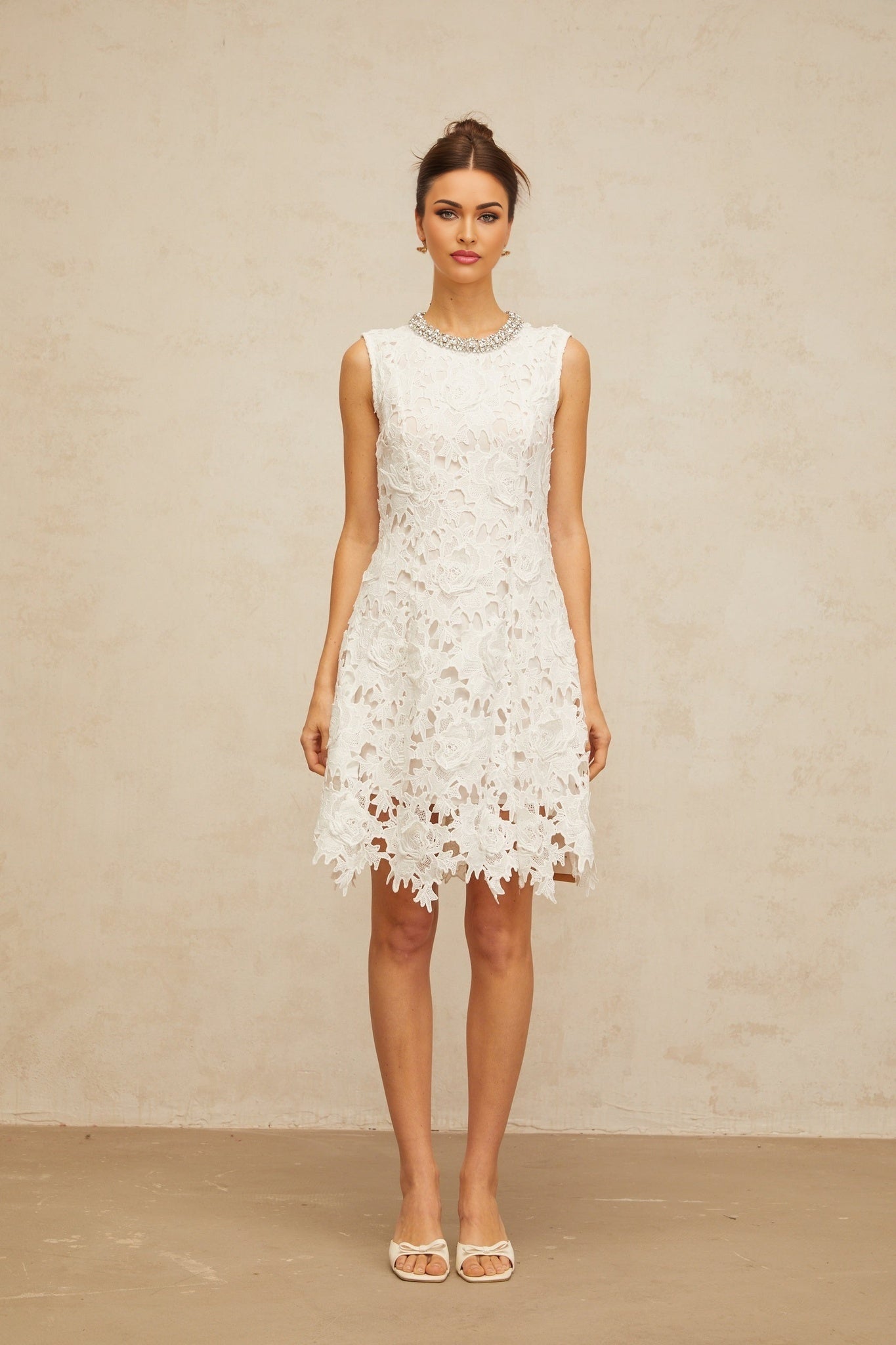 A short white mini dress with intricate corded lace details and embellishments featuring a delicate floral pattern and feminine silhouette