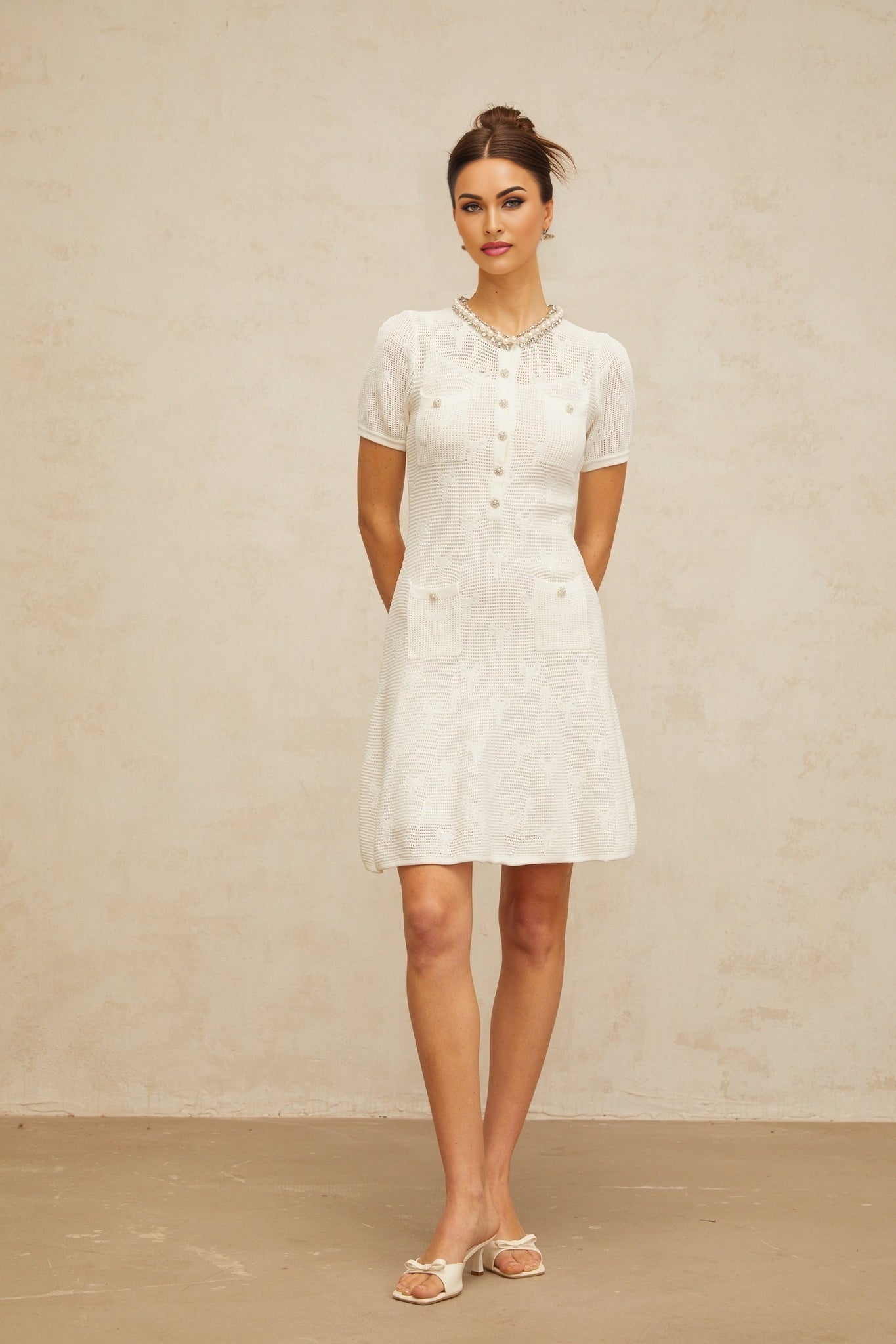 A short white mini dress with intricate crochet knit pattern and embellishments featuring a delicate Marjolaine design