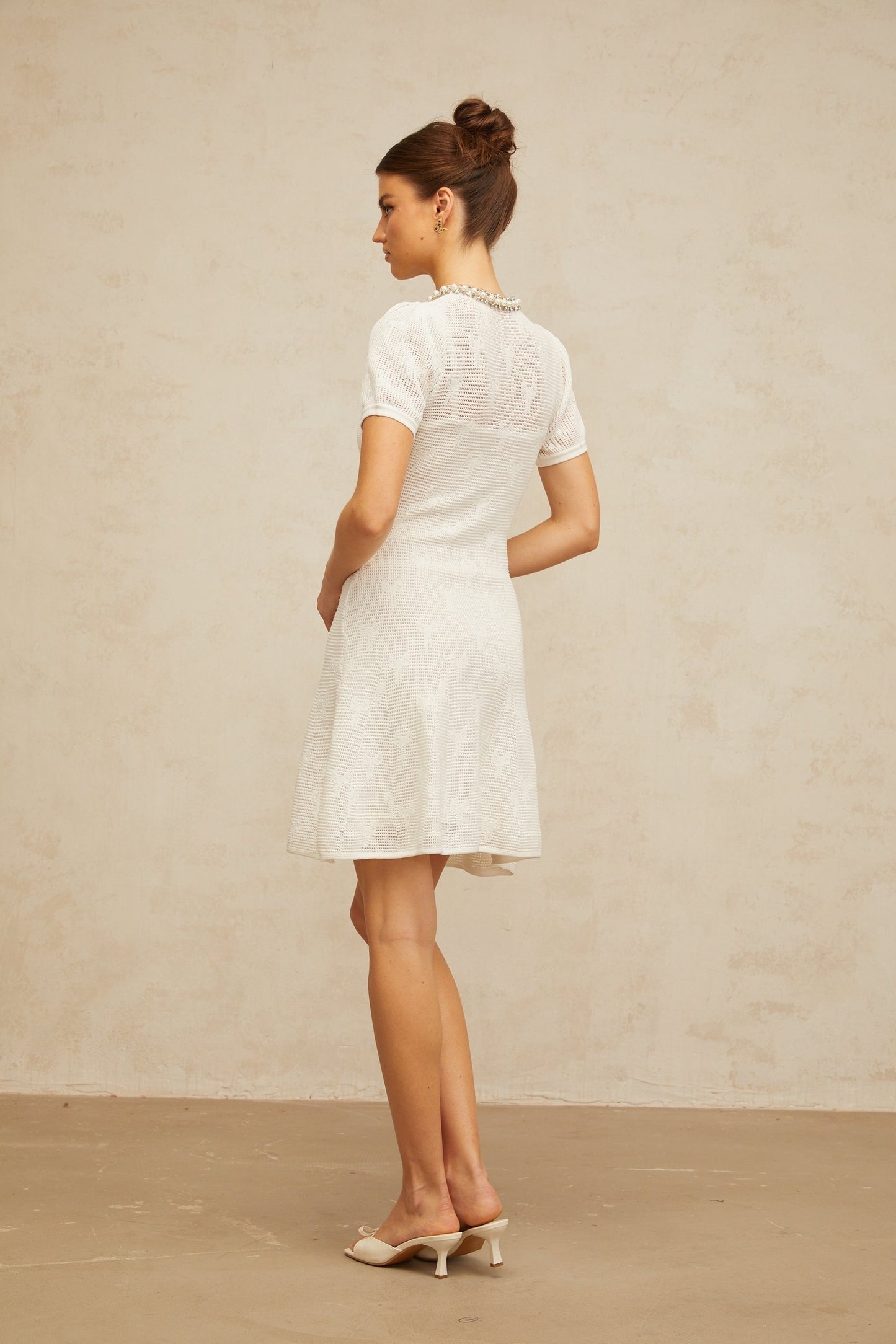 A short white mini dress with intricate crochet knit pattern and embellishments featuring a Marjolaine design