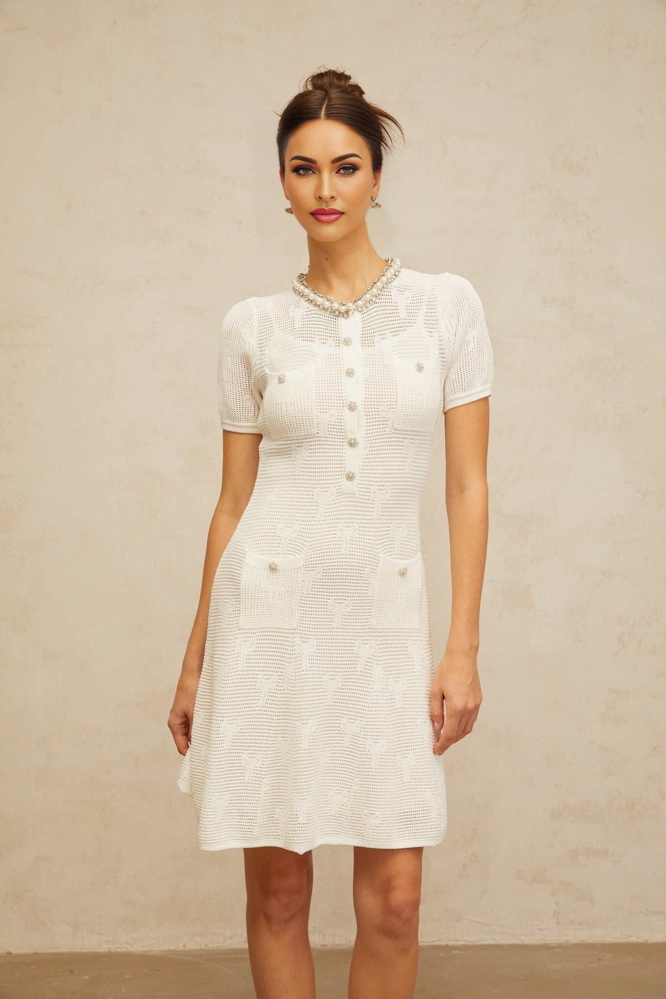 A short white mini dress with intricate crochet knit pattern and embellishments featuring a Marjolaine design