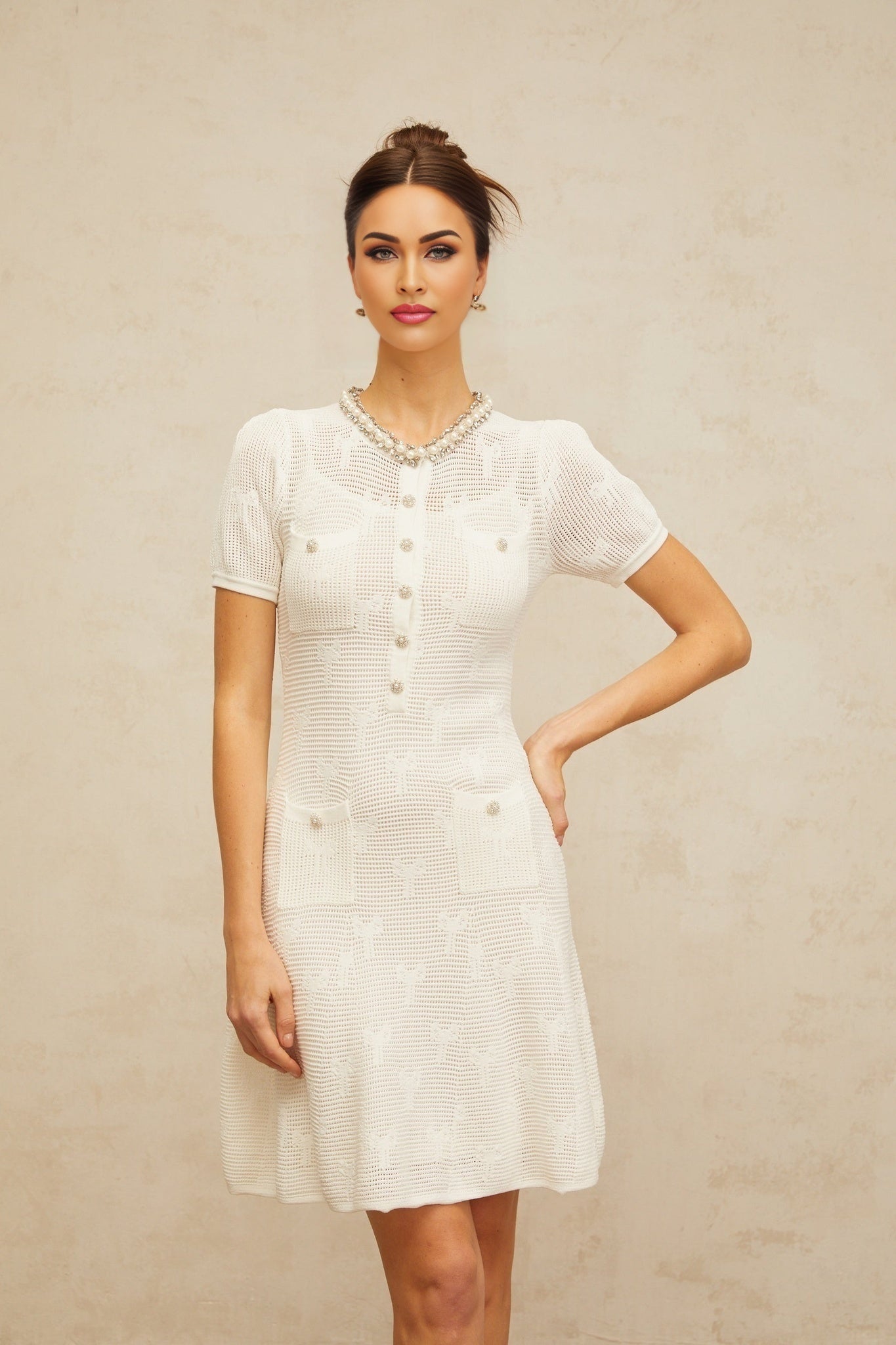 A short white mini dress with intricate crochet knit patterns and embellishments featuring a delicate Marjolaine design