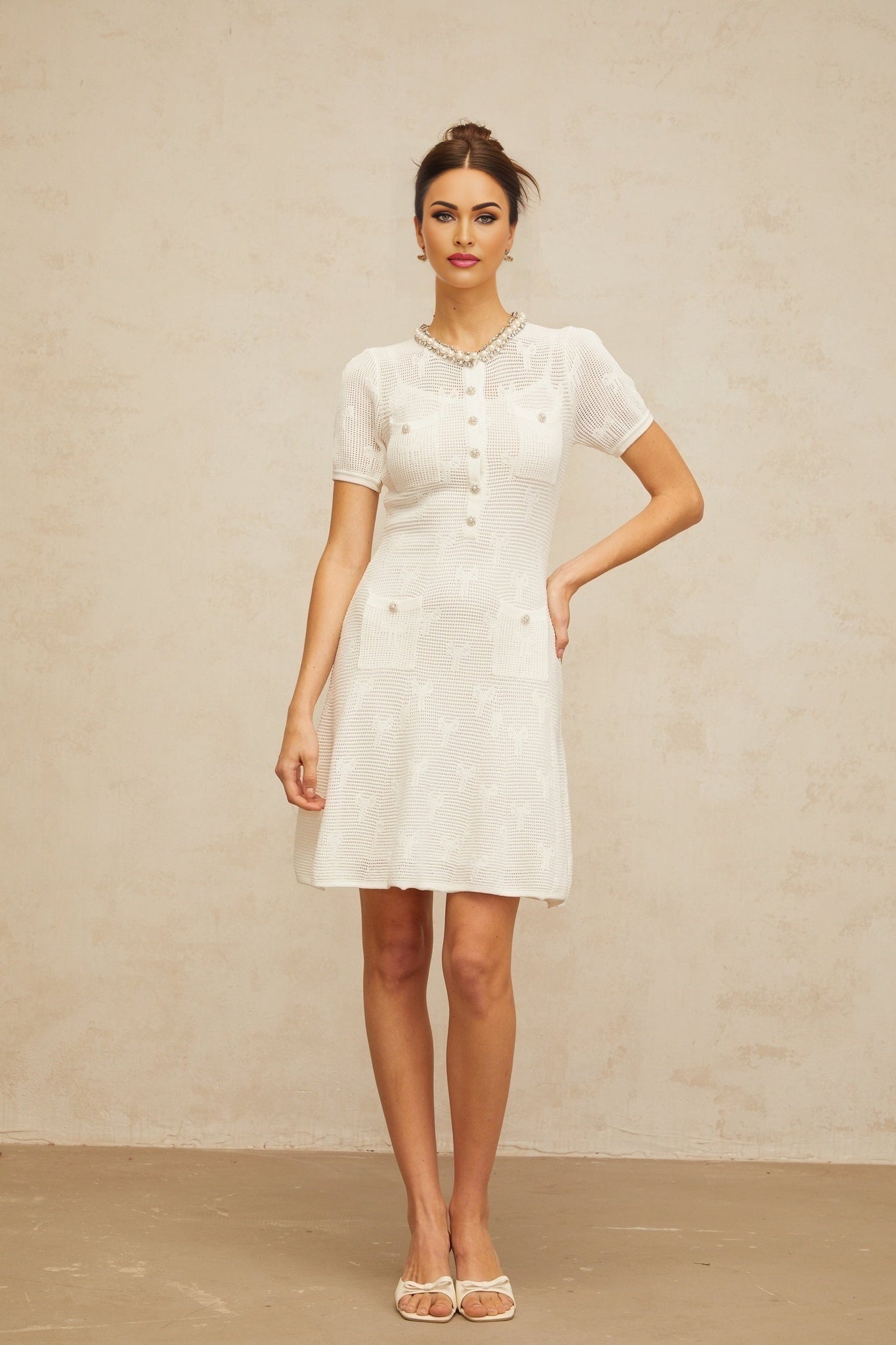 A short white mini dress with intricate crochet knit patterns and embellishments featuring a delicate Marjolaine design