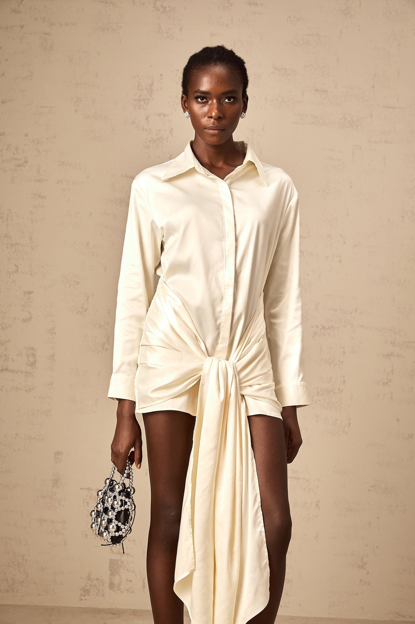 A short white mini dress with ruched details and a ribbon accent featuring a shirtstyle design and called Daphne