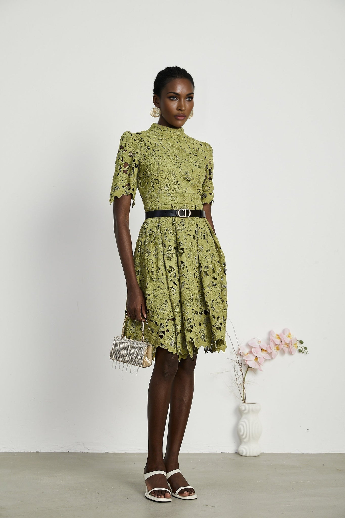 A short white minidress with embroidery details and cutout sections worn by a model standing against a plain background