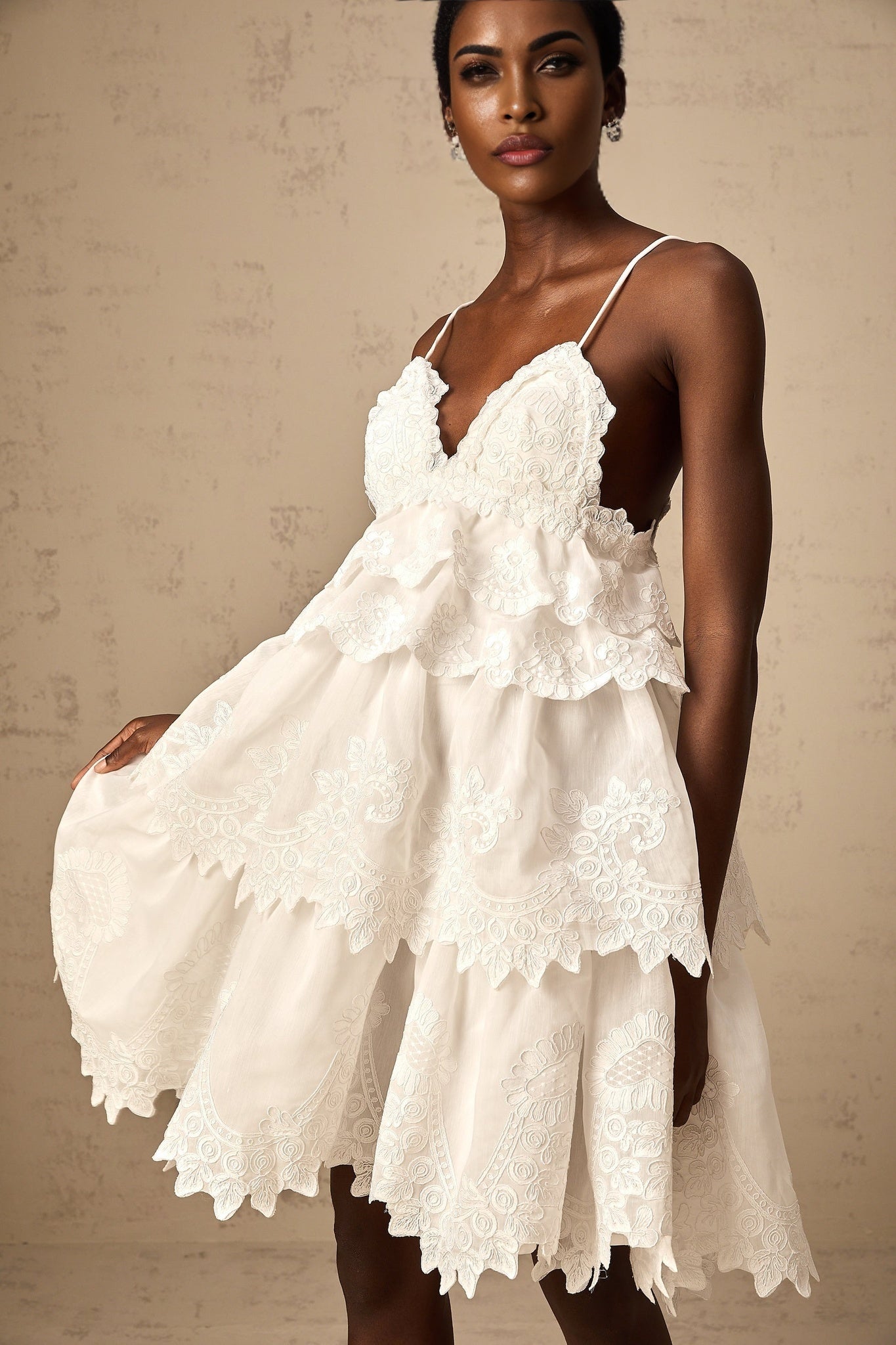 A short white tiered mini dress with intricate guipure lace detailing throughout featuring a fitted bodice and flared skirt