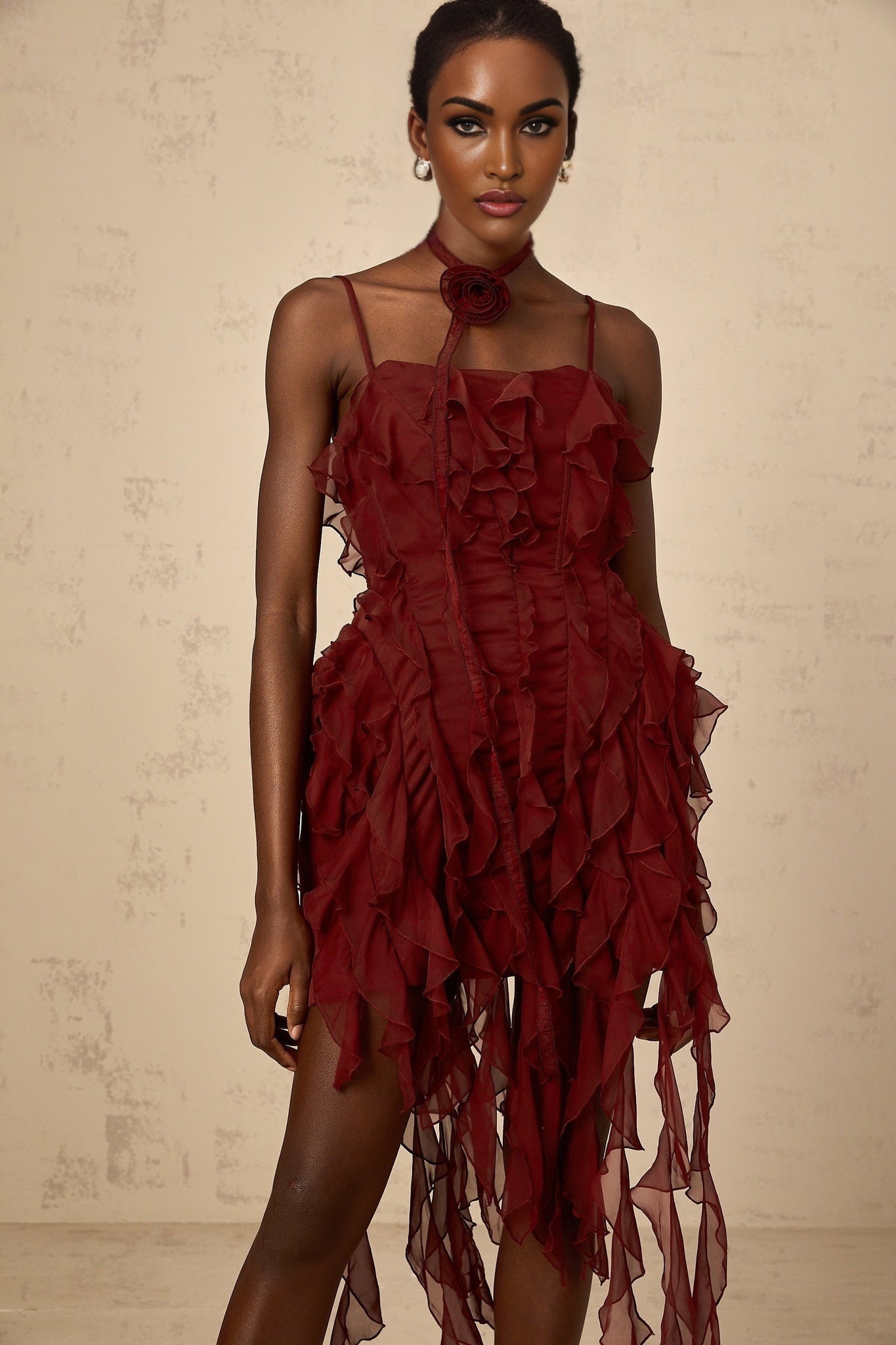 A short winered dress with ruffled details and rose appliques on a model against a plain background