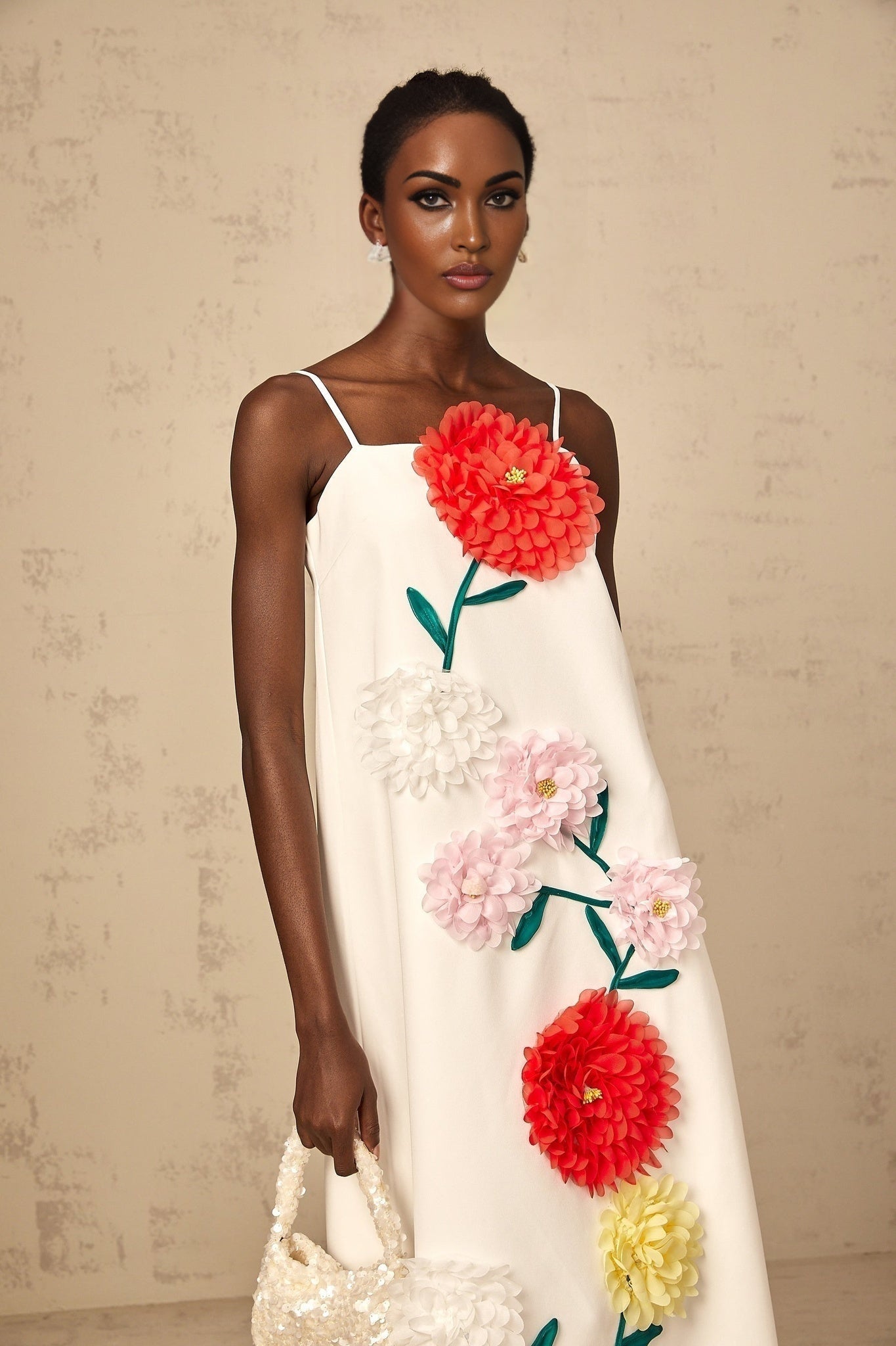 A sleeveless white midi dress with three dimensional floral petal details covering the bodice