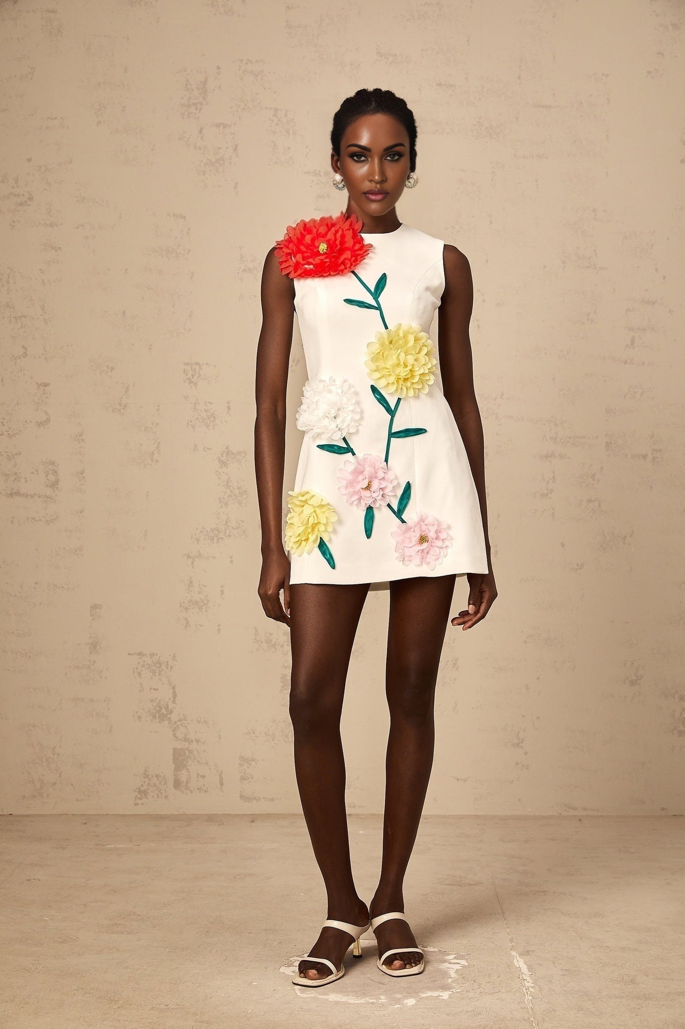 A sleeveless white mini dress with three dimensional petal details on the fabric worn by a model against a plain background