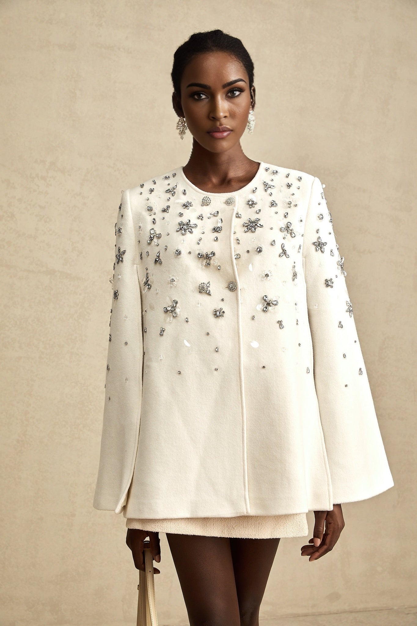 A stylish white jacket with a cape design featuring embellishments and elegant draping