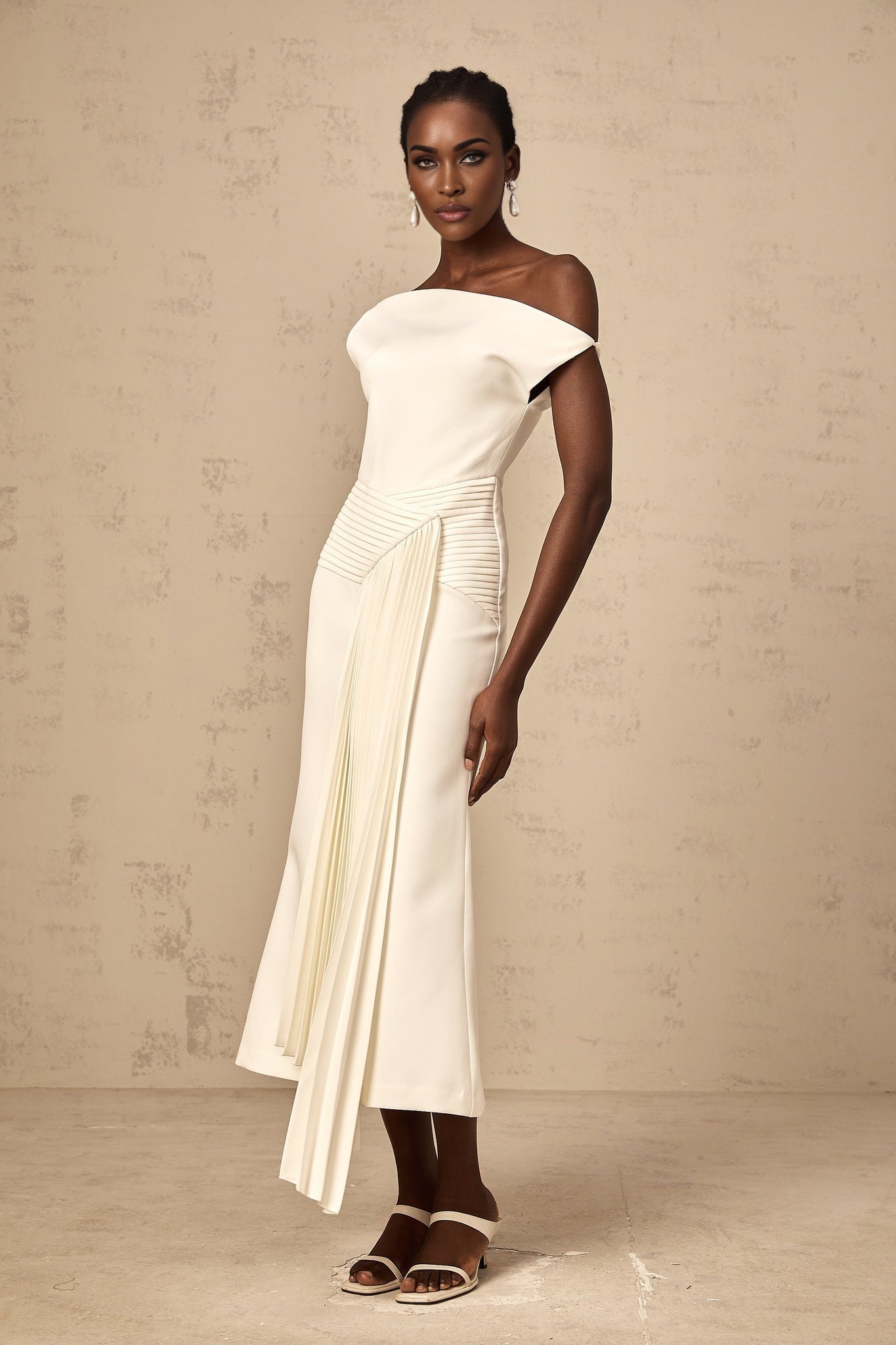 A white asymmetric midi dress with draped fabric details worn by a model standing against a plain background