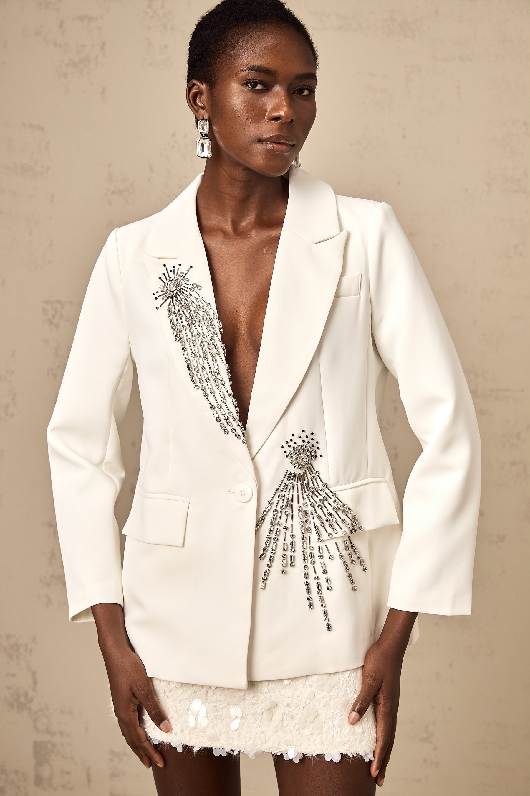 A white blazer adorned with crystal embellishments featuring a tailored fit and elegant design