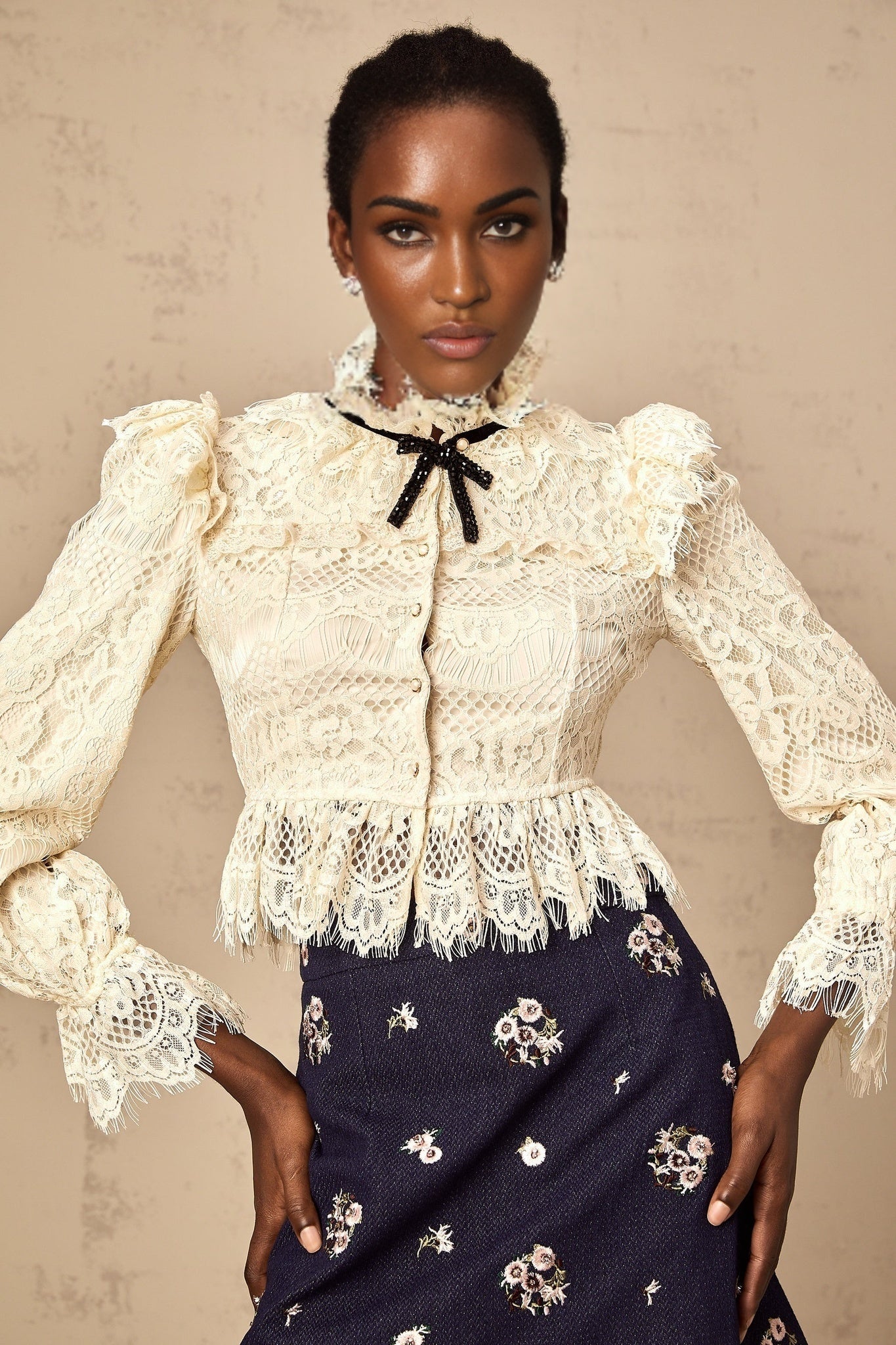 A white blouse with a bow detail at the neckline and delicate floral lace pattern throughout the garment