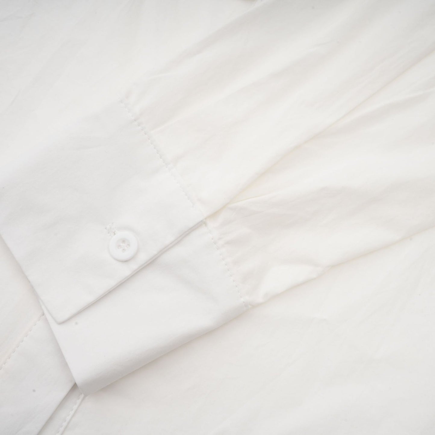 A white buttonup shirt with floral cutout patterns visible on the sleeves and body featuring a relaxed fit and collar