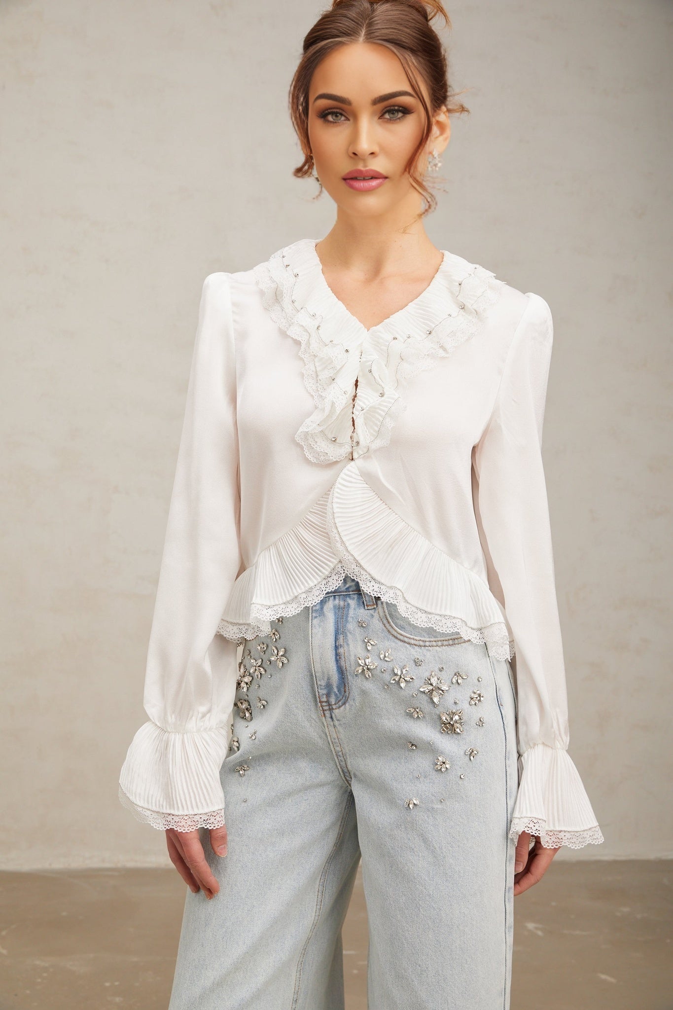 A white buttonup shirt with lace trim and ruffled details on the sleeves and collar